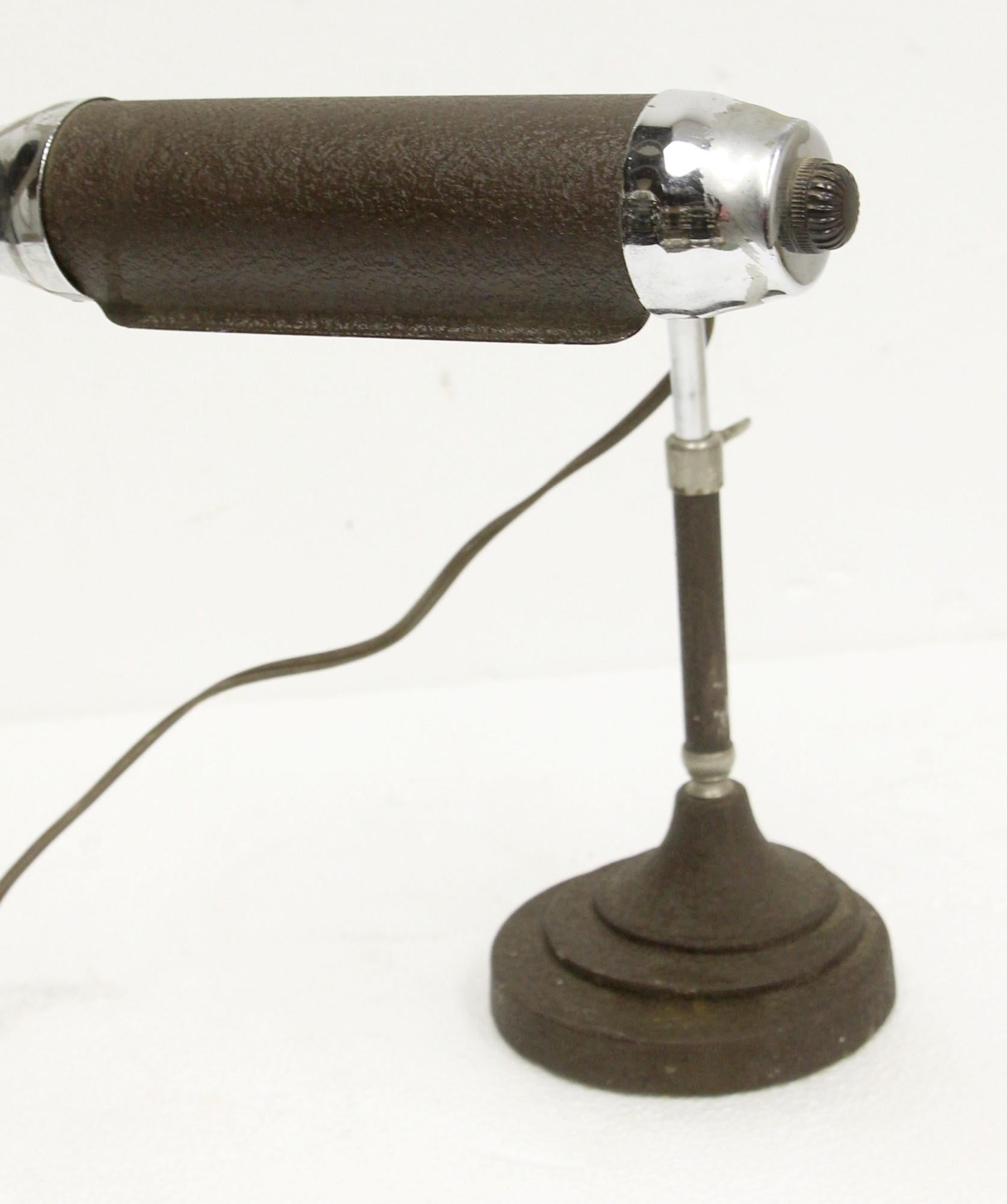 This 1950s vintage piano desk lamp is in the Art Deco style. The finish is a textured brown enamel with a deco base, along with chrome ends in the skyscraper design. The lamp is adjustable, and it takes a long tubular screw in bulb. This can be seen