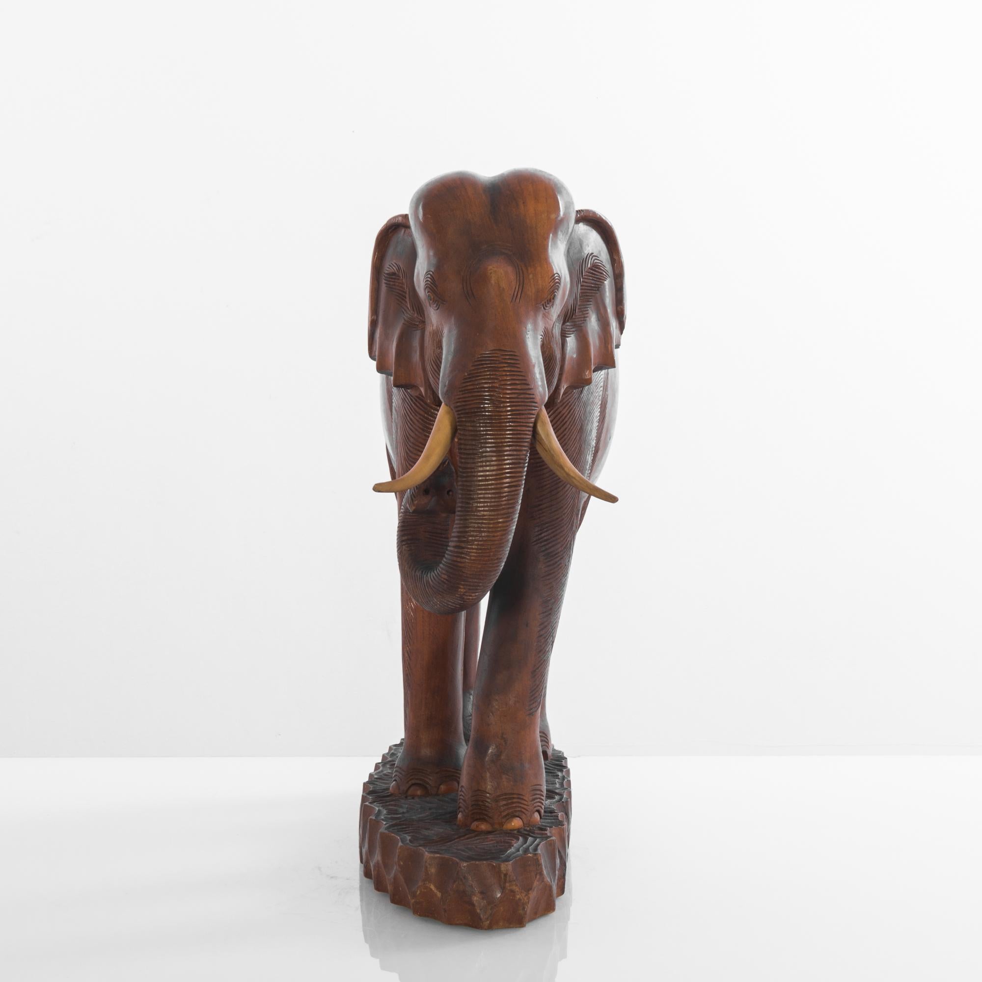 Questo elefante africano in legno del 1950 è una squisita rappresentazione dell'artigianato tradizionale. La figura, scolpita con meticolosa attenzione ai dettagli, mostra una patina ricca e calda che solo il tempo può donare. Le sue zanne