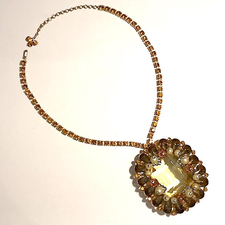 A beautiful vintage 1950s rhinestone pendant necklace. A large 1.25 inches wide and 1.5 inch high jonquil yellow emerald cut glass stone is is mounted in a gold tone setting. The stone is surrounded by amber pear rhinestones, small gold rhinestone