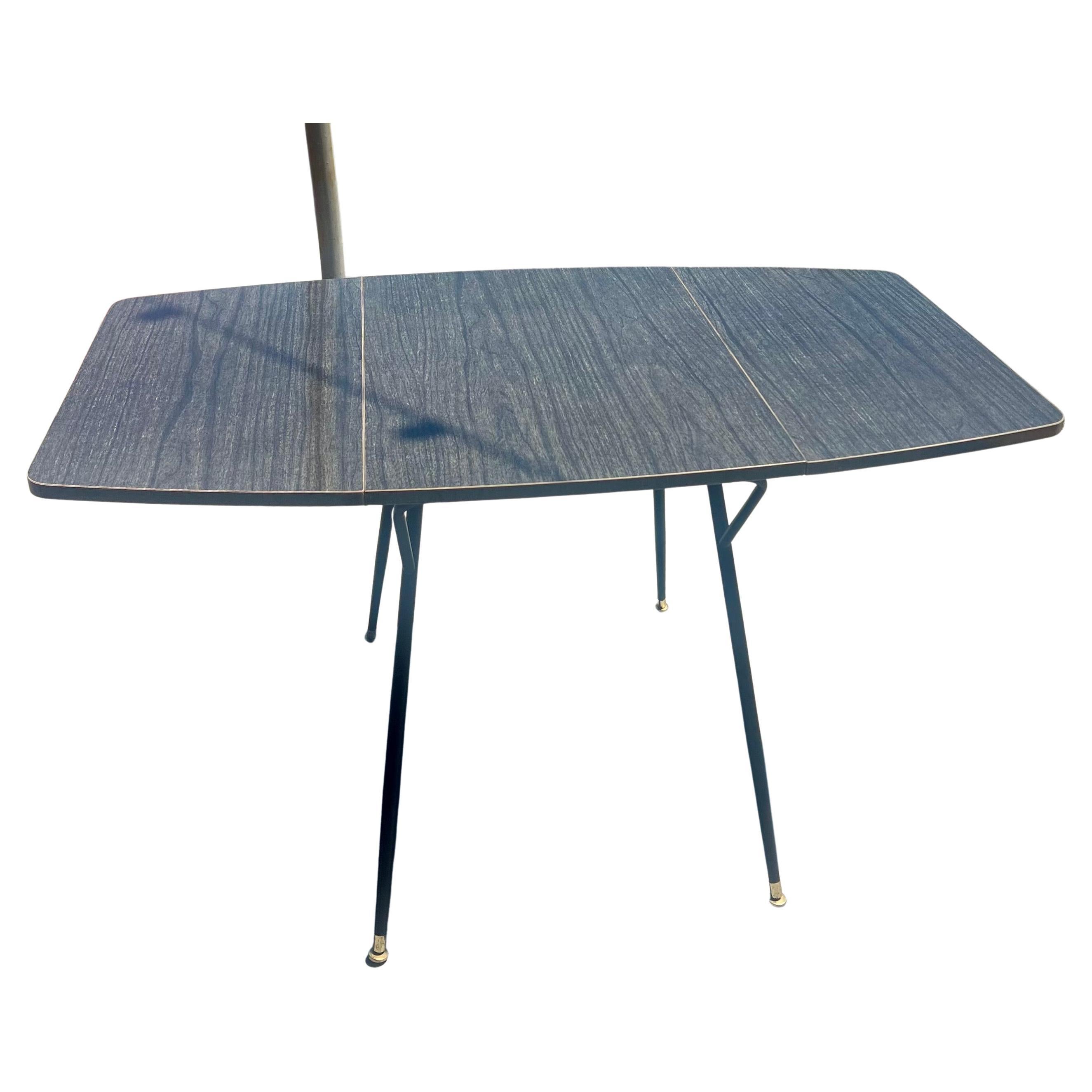 Table de dinette pliante en stratifié des années 50, en très bon état, en provenance du Mid Century Atomic age. Pièce rare, polyvalente et unique, pratique pour le rangement. Jolis pieds tubulaires émaillés noirs avec capuchons en laiton, en très