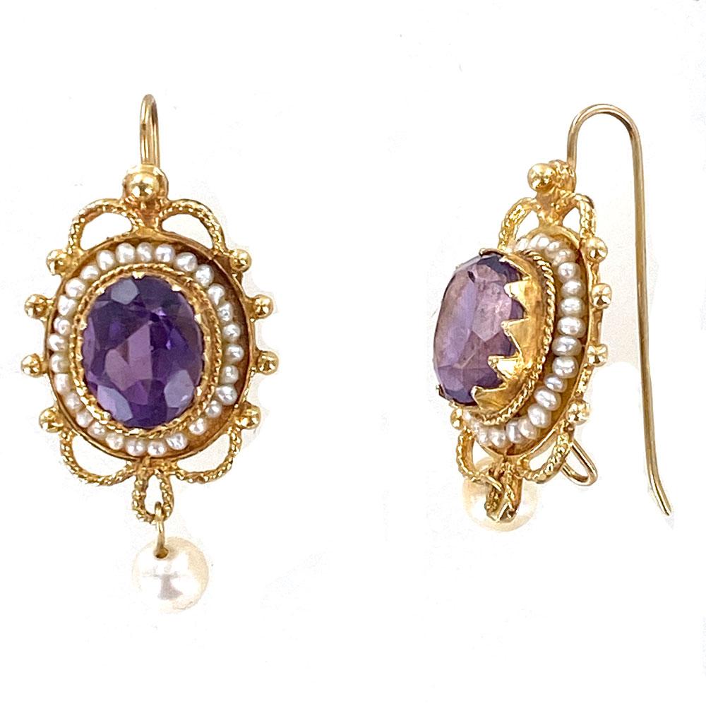 Stunning amethyst and seed pearl drop earrings circa 1950's. The earrings feature two faceted  oval amethyst drops with surrounding seed pearls. A single white pearl drops from each earring. The earrings are fashioned in 14 karat yellow gold and