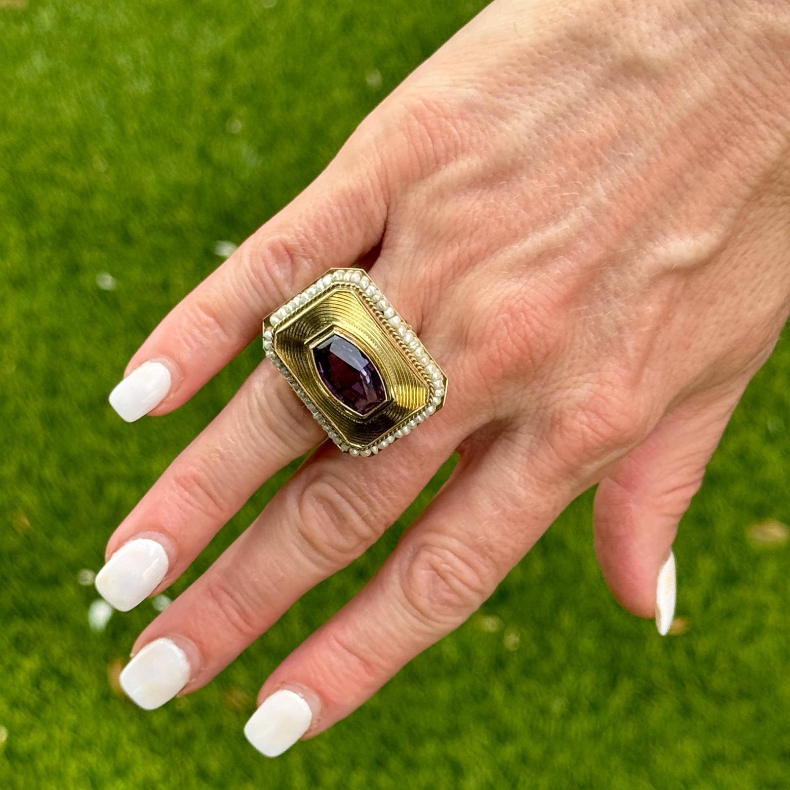 This exquisite statement ring from the 1950s showcases a striking amethyst, its rich, deep purple hue drawing immediate attention. The amethyst is beautifully complemented by a delicate halo of seed pearls, each one meticulously set to enhance the