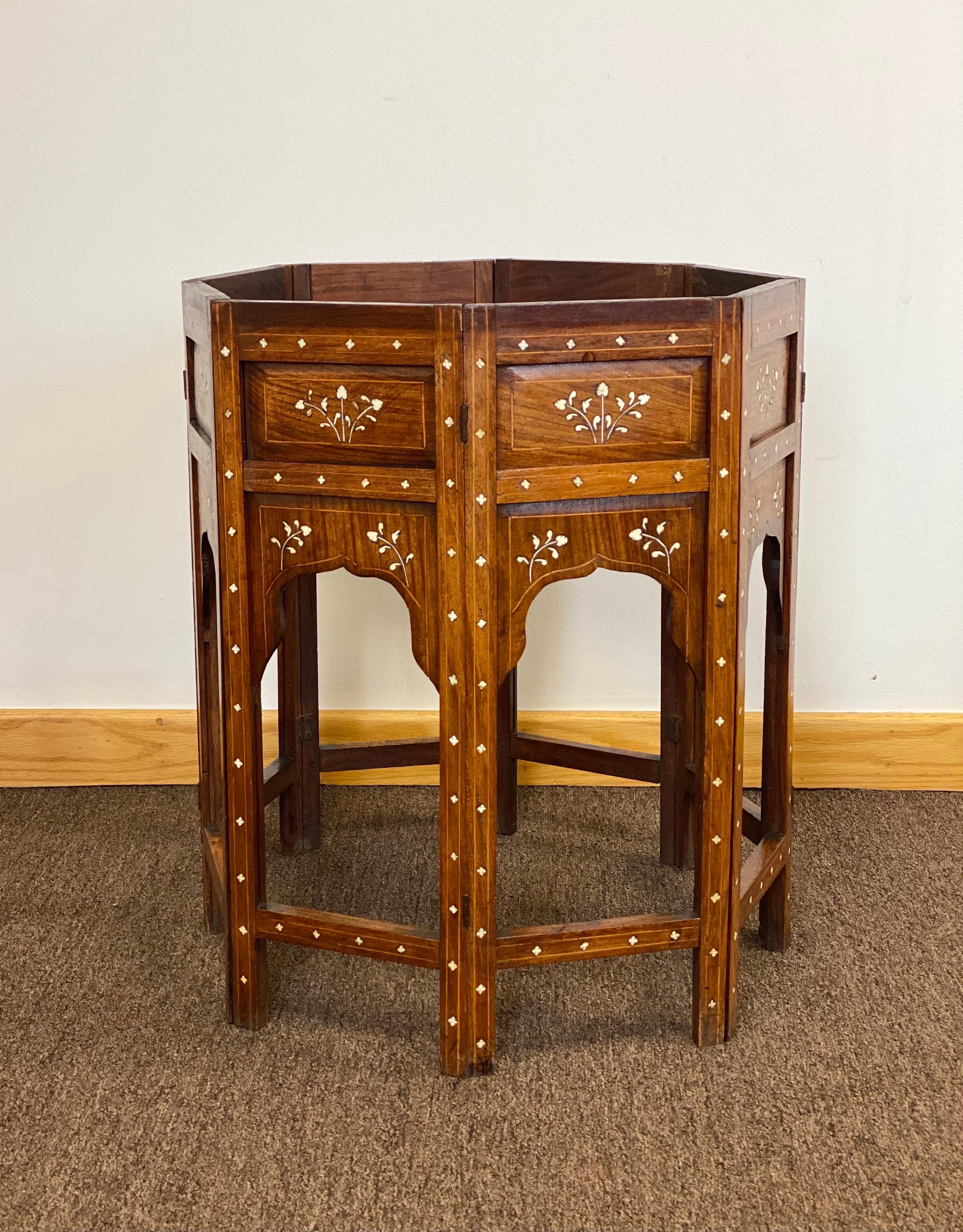 We are very pleased to offer a beautiful side tea table, circa the 1950s. Handcrafted from solid wood, this gorgeous piece showcases an intricate bone inlaid that displays a beautiful visual contrast. The folding base showcases eight arched panels