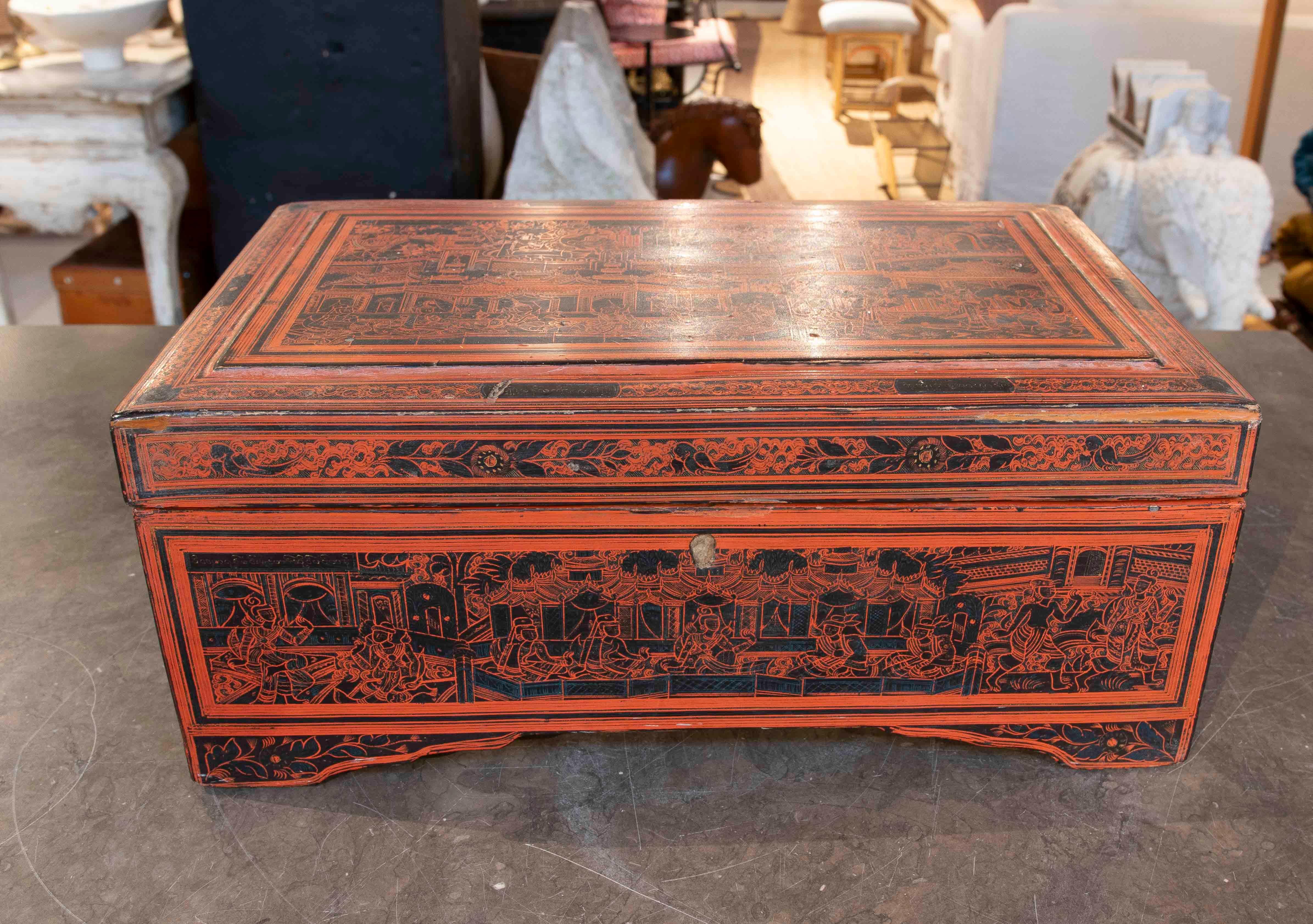 A beautiful antique wooden box lacquered in reddish and black tones, decorated with intricate traditional motifs depicting ornamental scenes and patterns. This detailed design highlights its unique, handcrafted character, ideal for those who