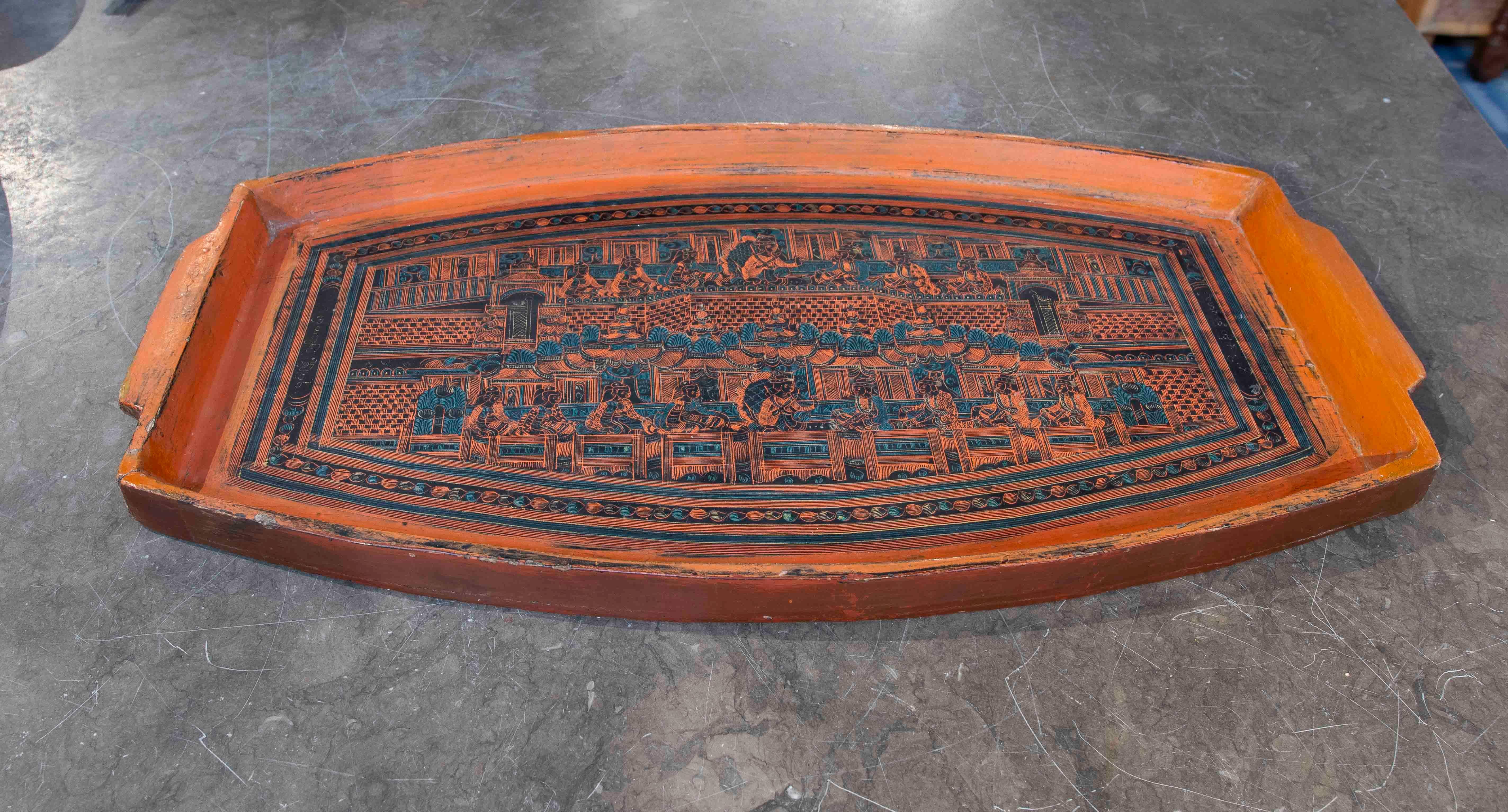 Magnifique plateau ancien en bois laqué dans les tons orange et noir, décoré de gravures complexes représentant des scènes traditionnelles et des motifs ornementaux détaillés. Son design artisanal reflète une esthétique unique et intemporelle qui en