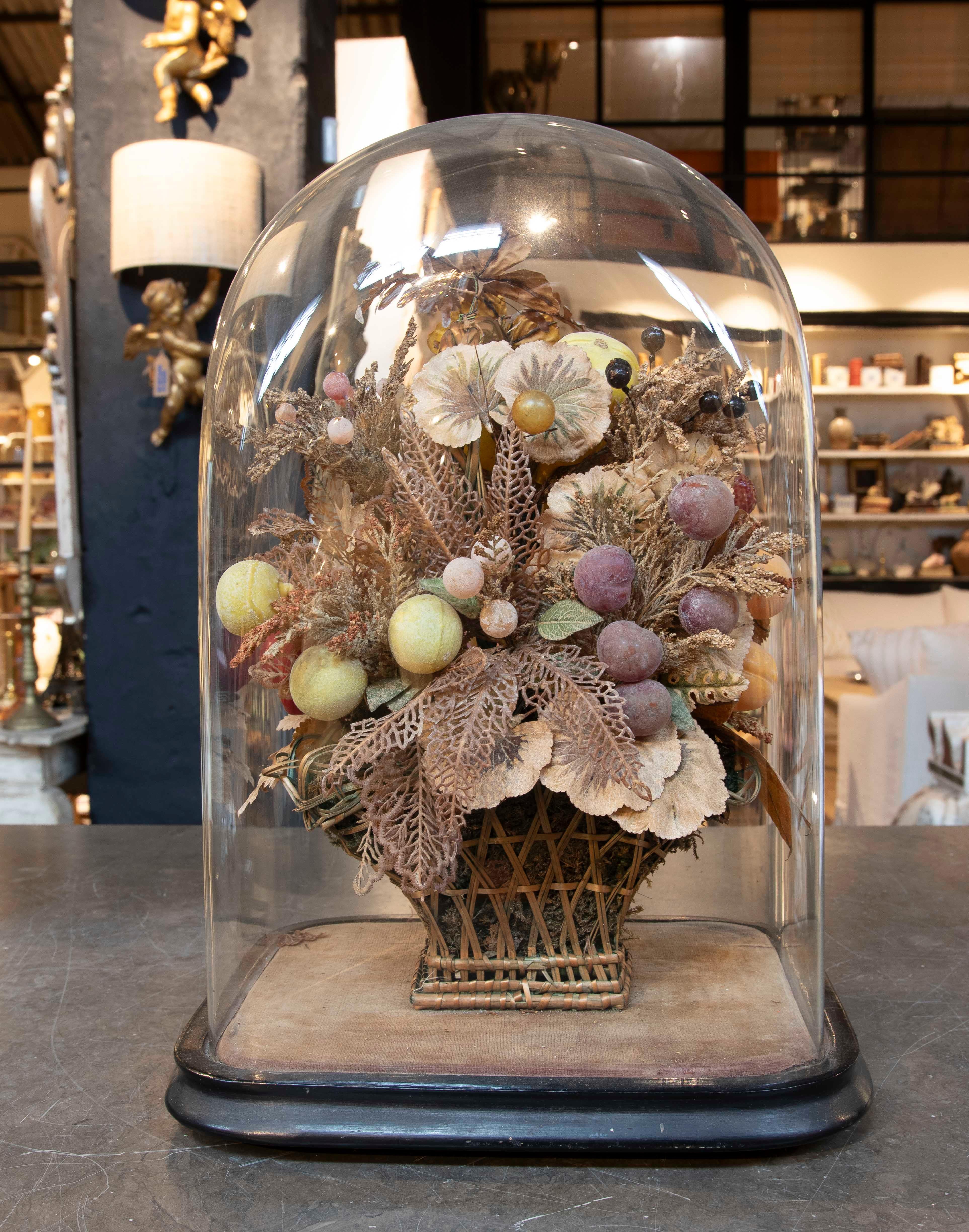 Un elegante e delicato centrotavola antico composto da una composizione di fiori e frutti secchi e artificiali, accuratamente disposti all'interno di una cupola di vetro su una base di legno. Questo pezzo cattura il fascino del romanticismo classico