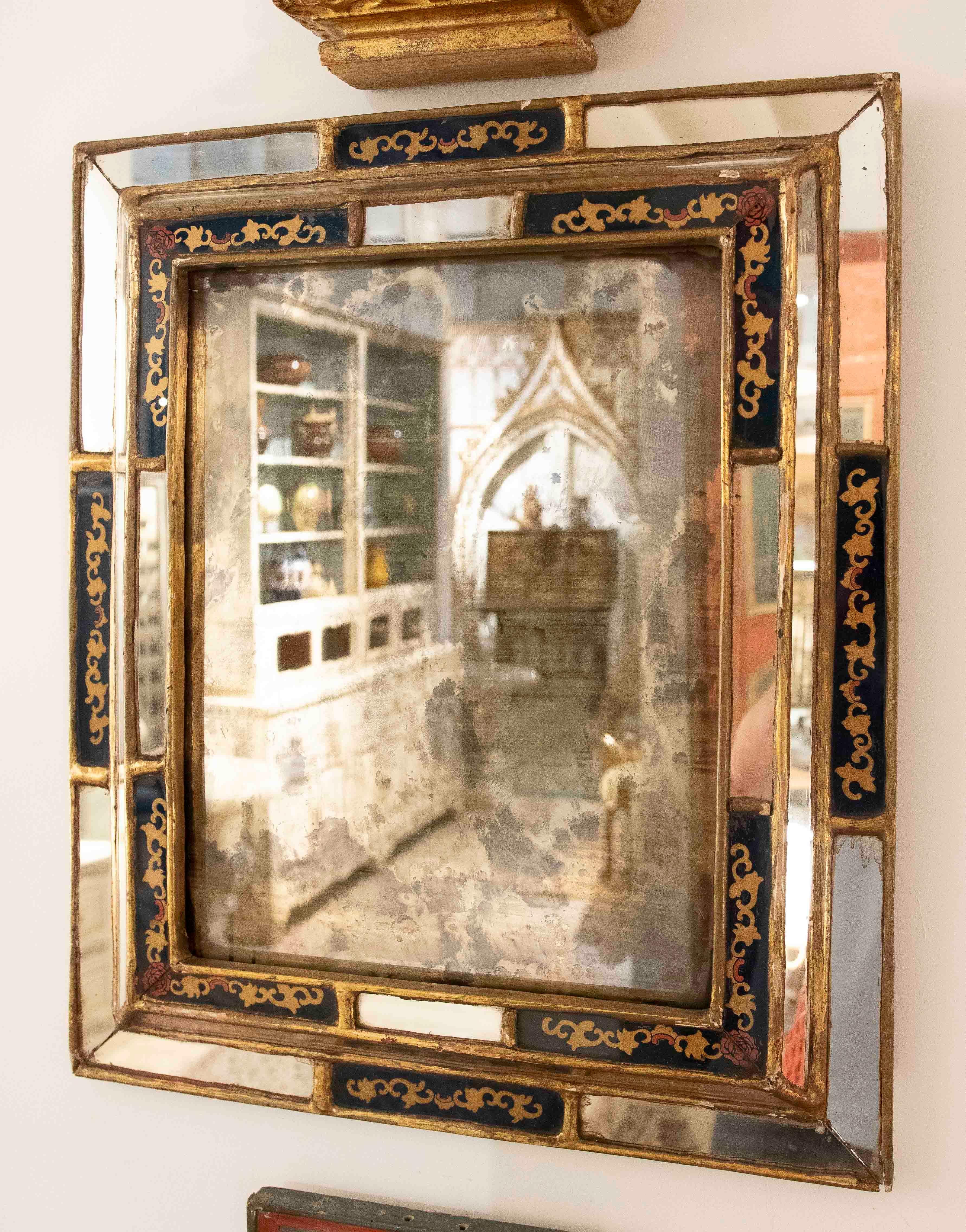 Charming vintage mirror with aged glass that provides a nostalgic and elegant aesthetic. Its rectangular frame is decorated with navy blue panels and hand-painted gold details, framed in gold leaf that enhances its classic character. Ideal for