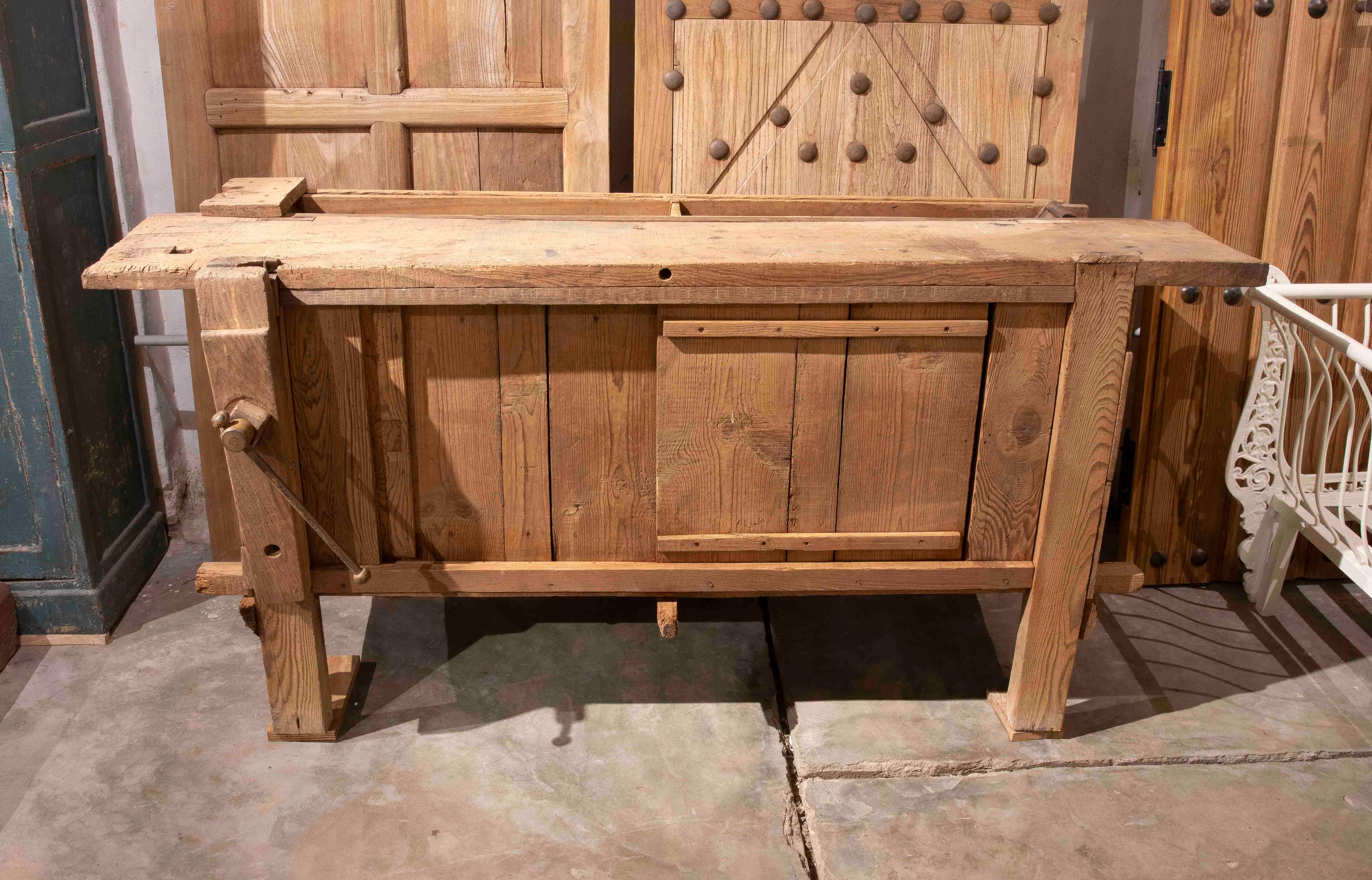 Authentique établi de charpentier du milieu du XXe siècle en bois massif. Cette pièce conserve sa patine d'origine et le charme d'une utilisation artisanale, avec des détails fonctionnels tels que l'étau latéral et la surface de travail spacieuse.