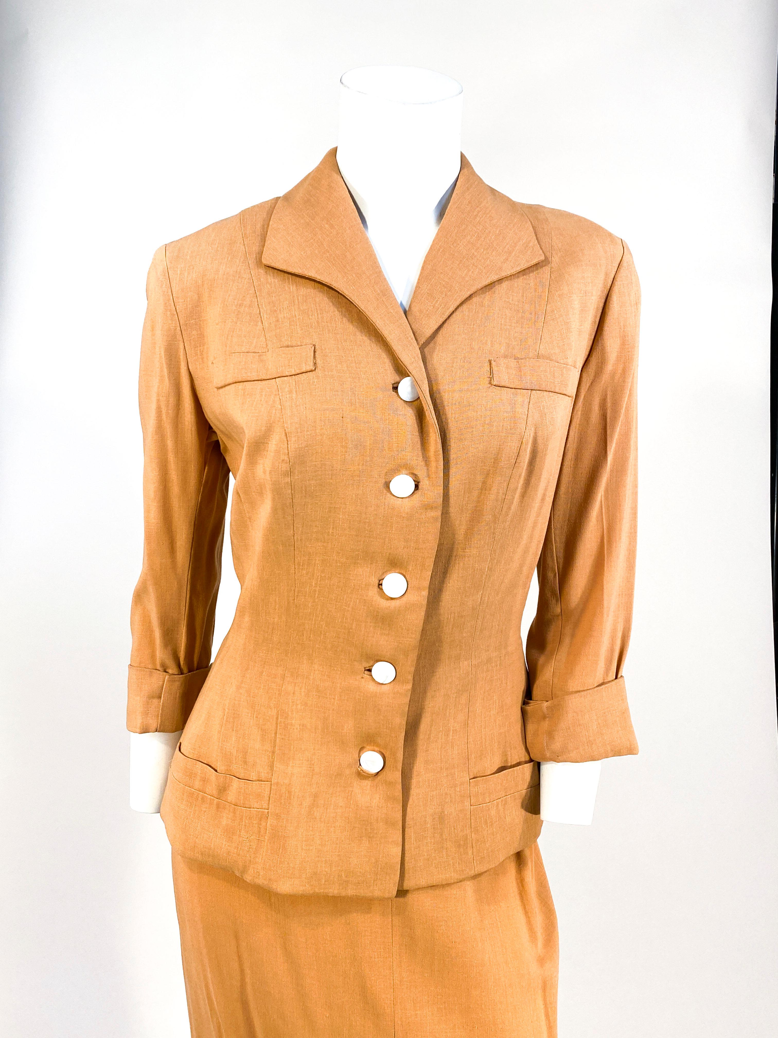 Early 1950s muted apricot colored linen suit with three-quarter length sleeves finished with a fold. The face of the jacket hat two faux pockets at the top, two shallow pockets at the bottom, and a row of large mother of pearl buttons with inset