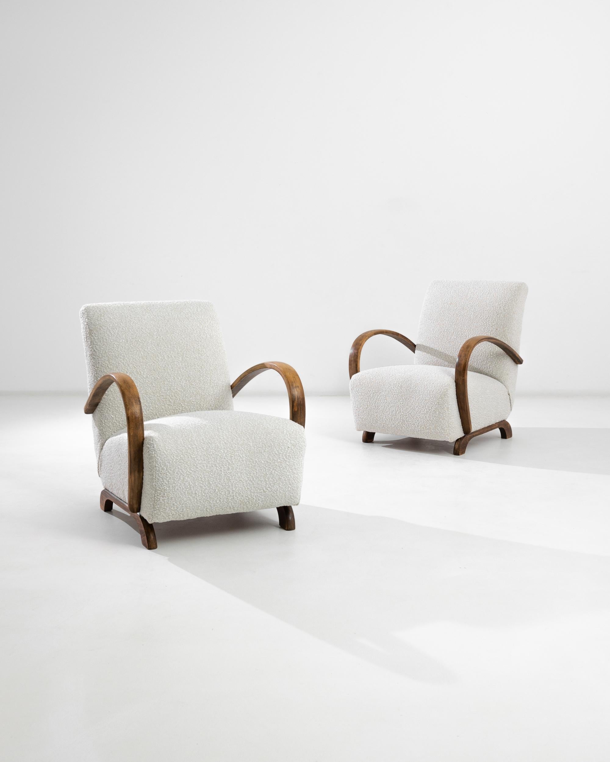 A pair of armchairs by Czech furniture designer Jindrich Halabala. This 1950s design is upholstered in an updated white boucé fabric, the textural neutral was chosen to compliment the embracing warmth of the brown hardwood frame. Influenced by