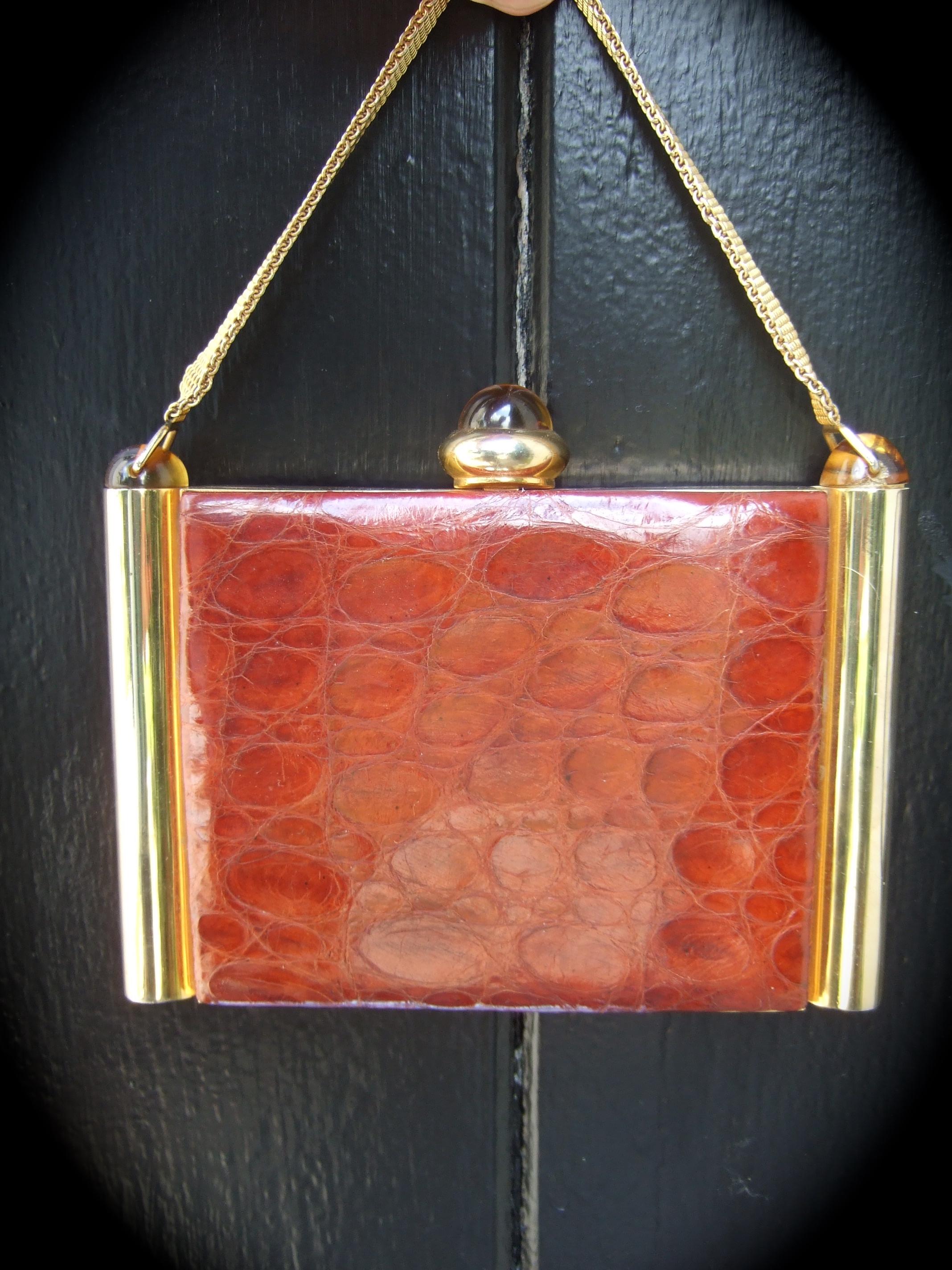 1950s Art Deco brown alligator evening bag - compact case 
The elegant evening bag is covered with brown alligator panels 
Designed with brass elongated cylinders that frame the sides 

Carried with a brass mesh chain strap. Adorned with amber