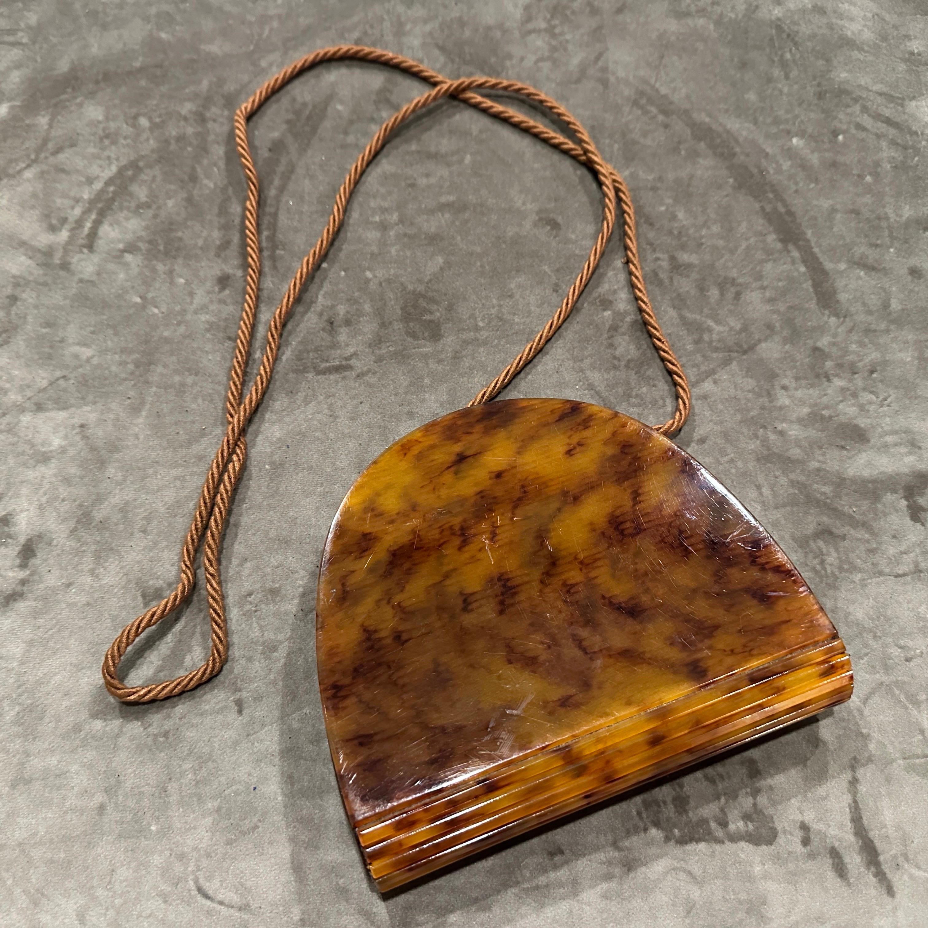 This vintage Italian handbag is a striking example of mid-century Bakelite craftsmanship, showcasing the elegance and experimentation of that era’s accessory design.
Made from richly marbled Bakelite in a deep amber tortoiseshell tone, this bag has