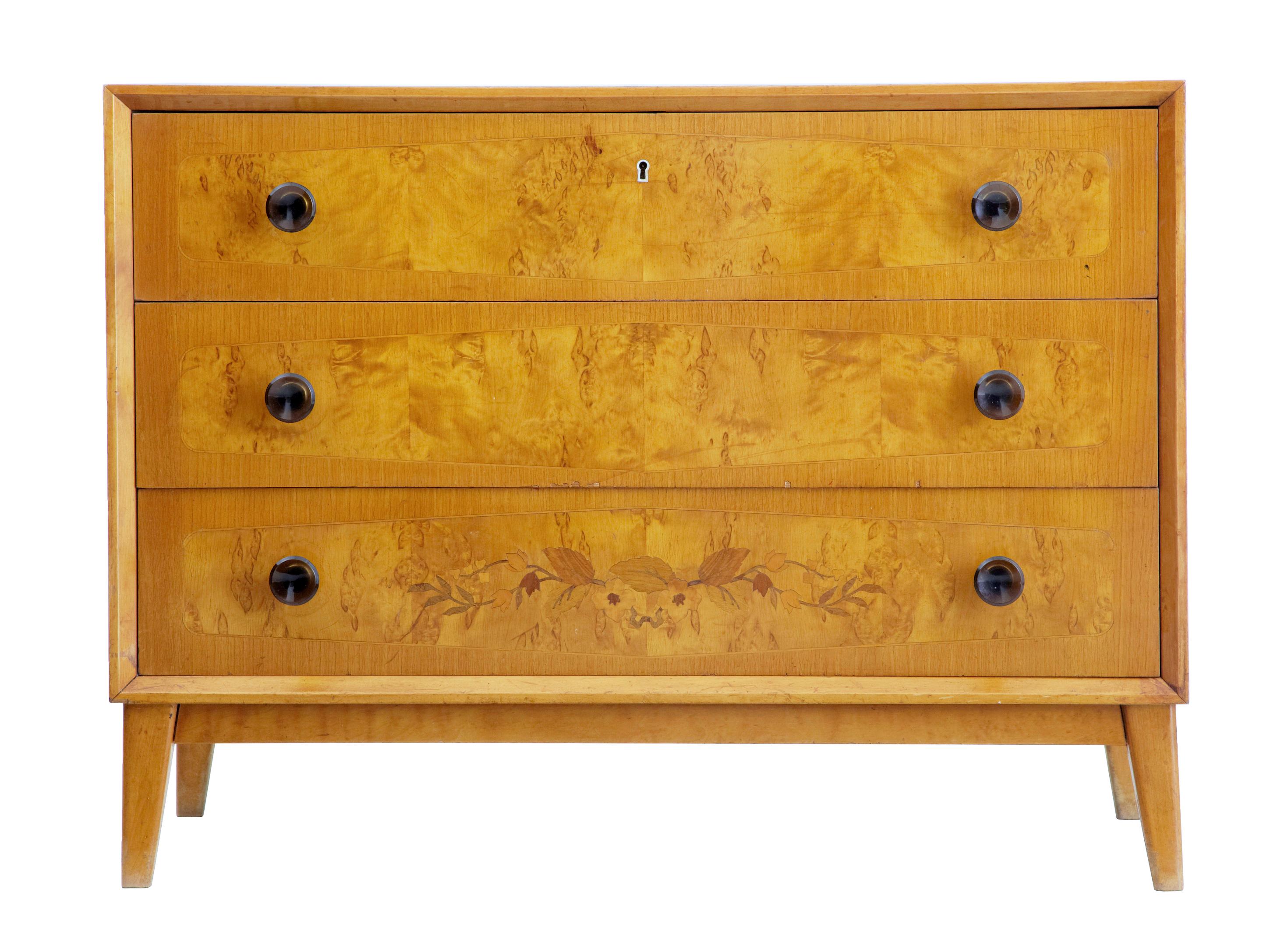 1950s Art Deco inspired birch inlaid chest of drawers

3-drawer chest with inlaid bottom drawer, circa 1950. crossbanded and strung drawer fronts, with faux colored glass handles. Standing on tapering legs. Good color and very stylish. Minor