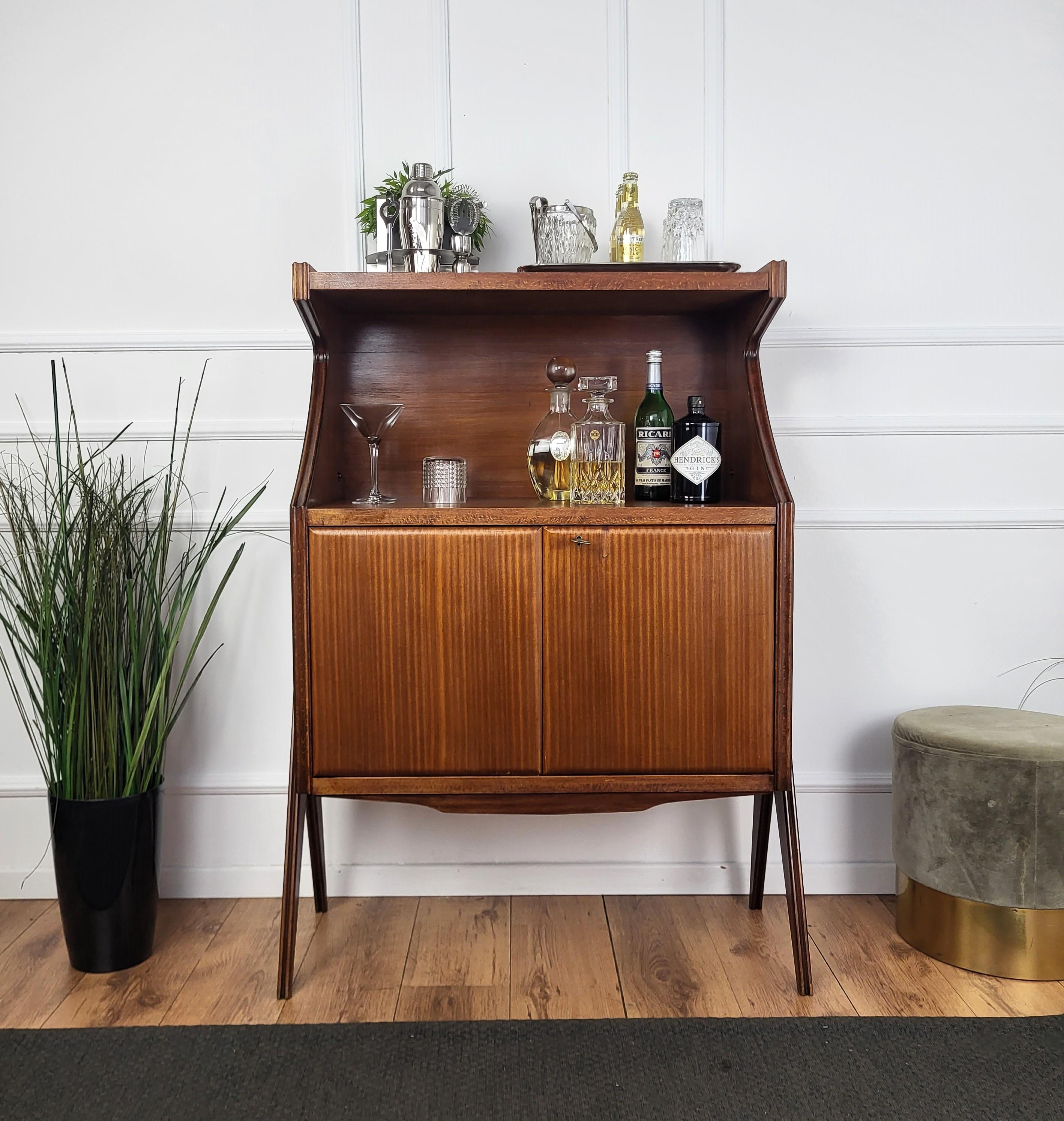 Very elegant Italian Art Deco Mid-Century Modern dry bar cocktail cabinet, in beautiful walnut veneer wood with central shelves and bottom door with internal storage and antique brass keylock, standing on two pairs of typical Italian Mid-Century