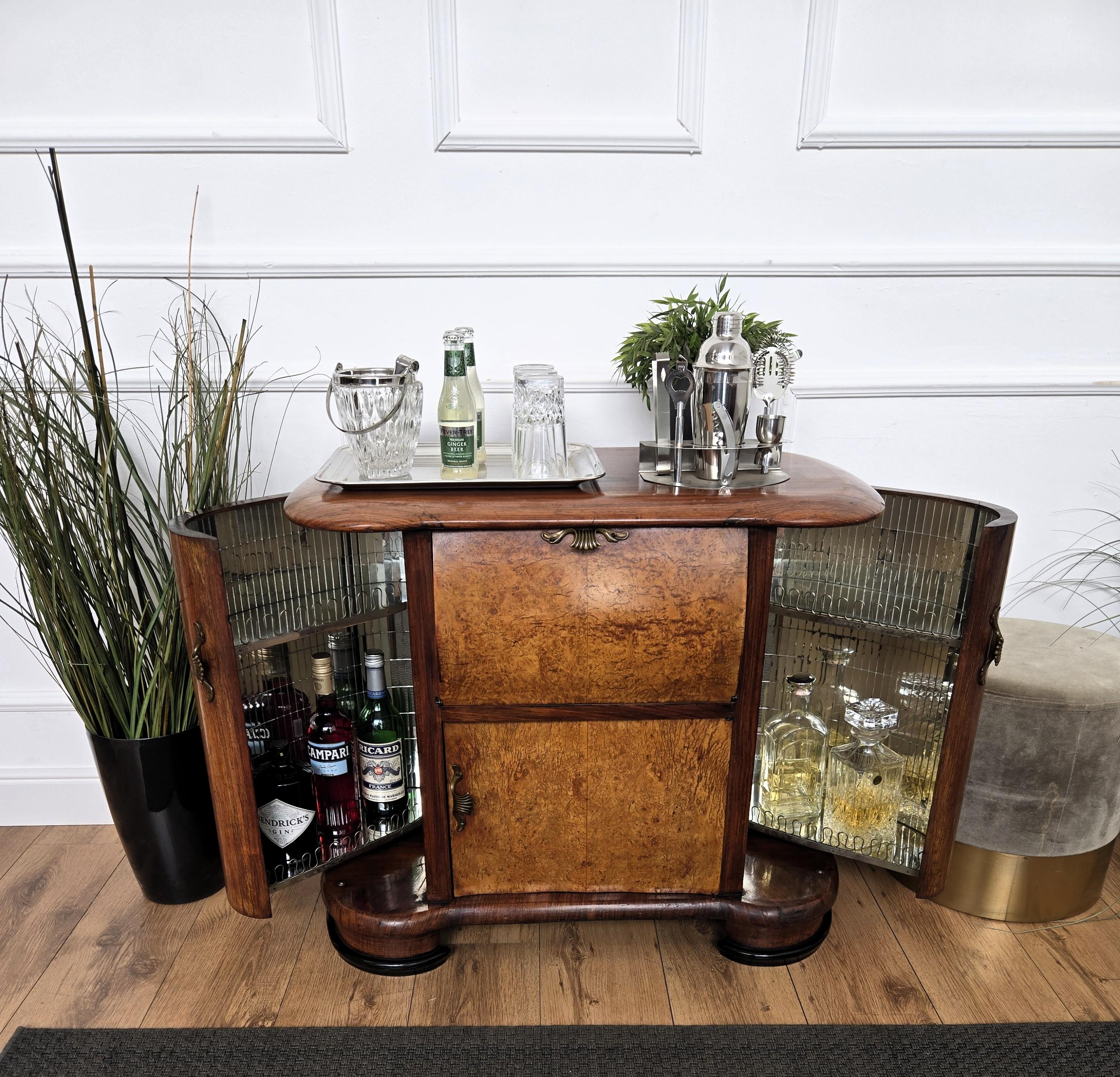 Elegantísimo mueble bar italiano Art Decó de mediados de siglo, en preciosa chapa de madera de nogal, con dos puertas y tiradores de latón antiguo. Cuando se abre, en los laterales aparece una sorprendente parte interior en mosaico de espejos y