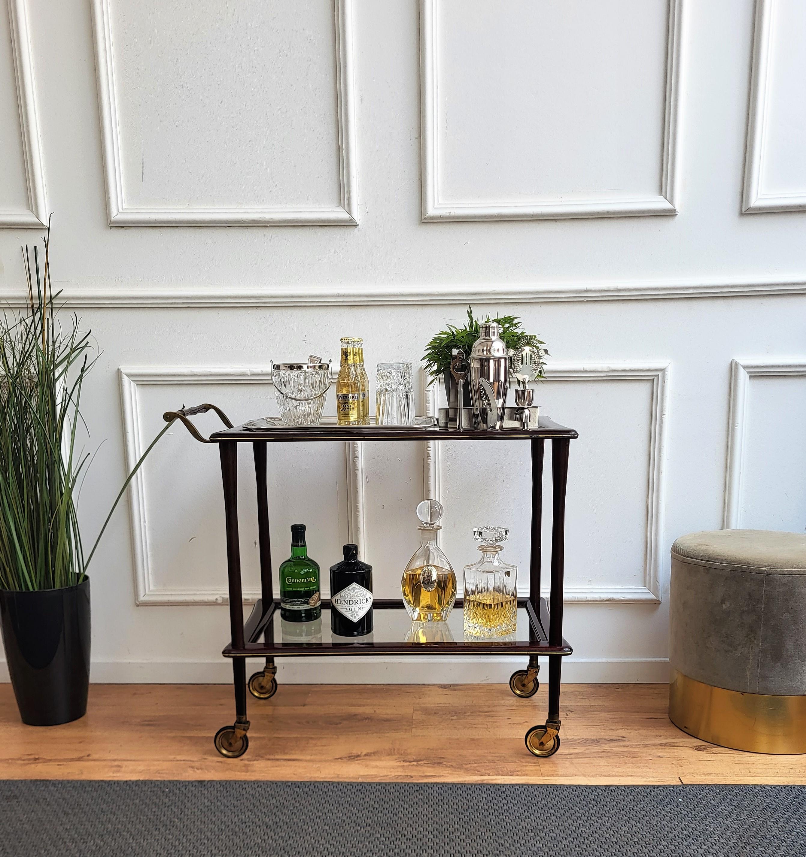 Unique and very elegant Italian Art Deco dry bar cabinet cart with two glass tiers and highlighted by the great wooden structure design and overall shape completed by the details of the brass decor frame and the brass handle and the original antique