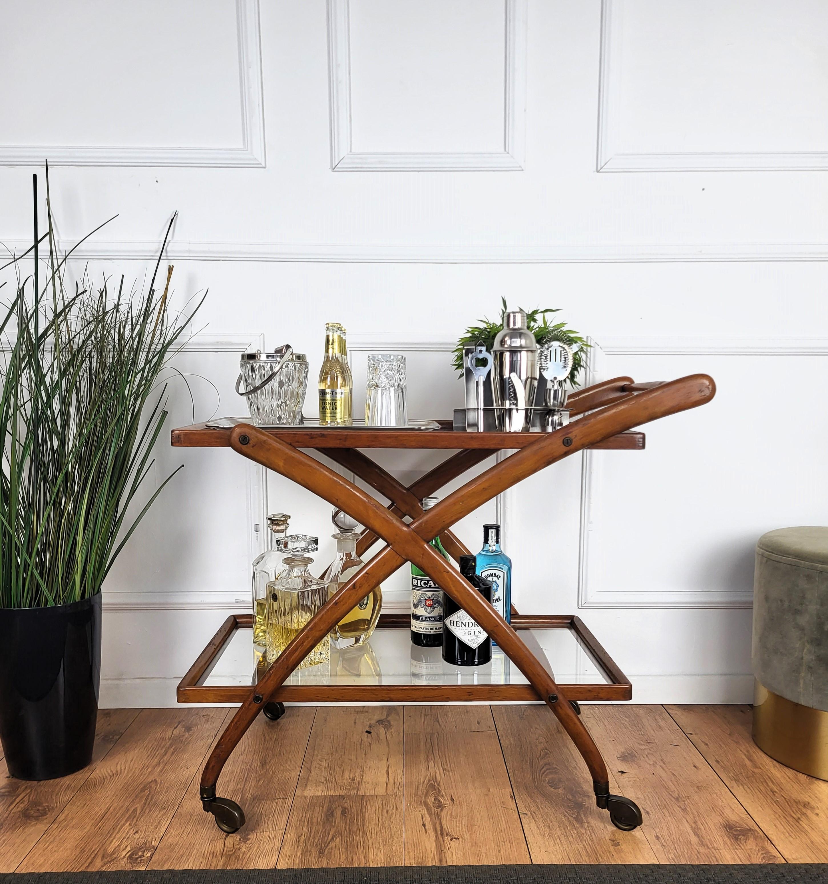 Unique and very elegant Italian Art Deco MidCentury Modern dry bar cabinet cart with two glass tiers and highlighted by the great wooden structure design and overall shape completed by the details of the original antique brass wheels. 

The Art Deco