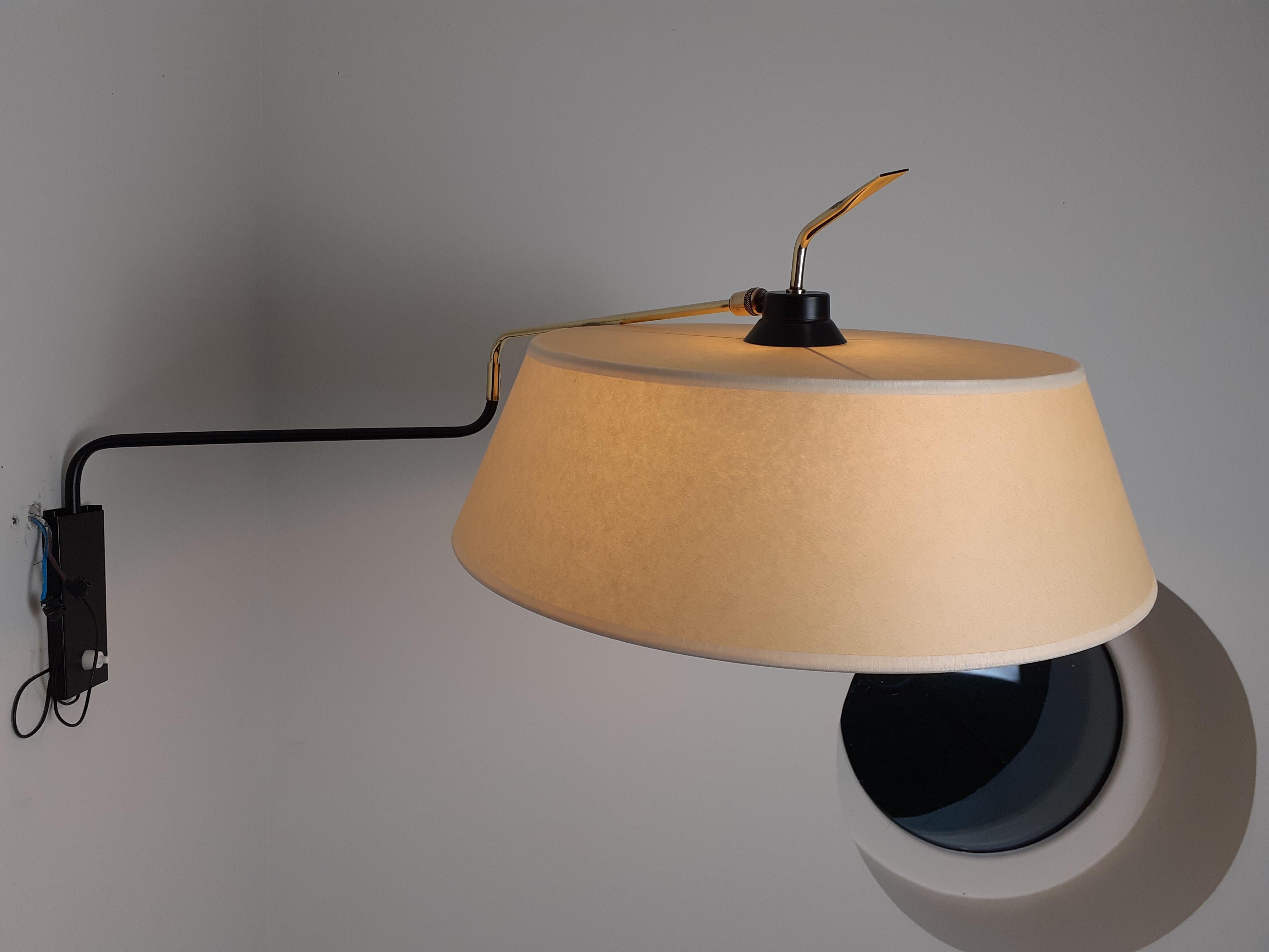 Wall lamp in black lacquered metal and brass, consisting of a rectangular base in black lacquered metal on which is arranged an arm of light in brass and lacquered metal.
The arm is articulated at its center and can be oriented.
It is finished by