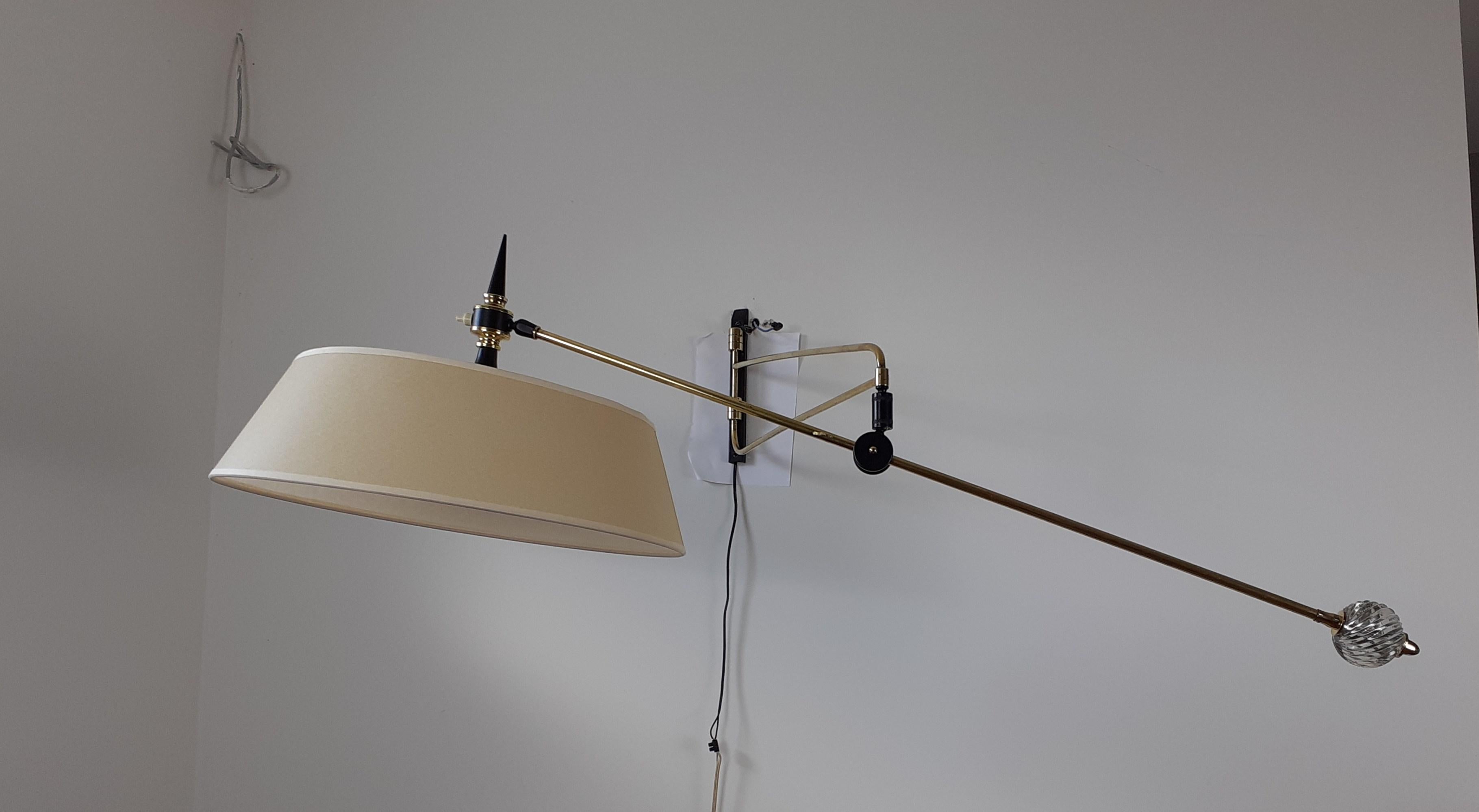 Wall lamp in black lacquered metal and brass composed of a rectangular base on which is fixed a double pivoting rod connected to an articulated brass arm. A glass ball allows the orientation and inclination of the arm of light.
A circular