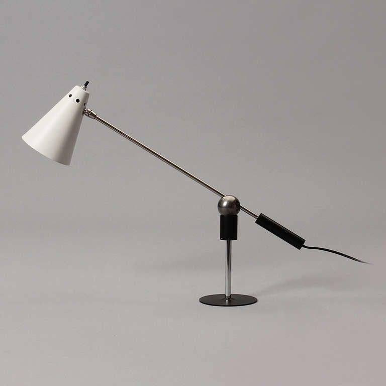 An articulating desk lamp with a cone shaped shade on a metal base and a magnetic ball connection to allow movement.