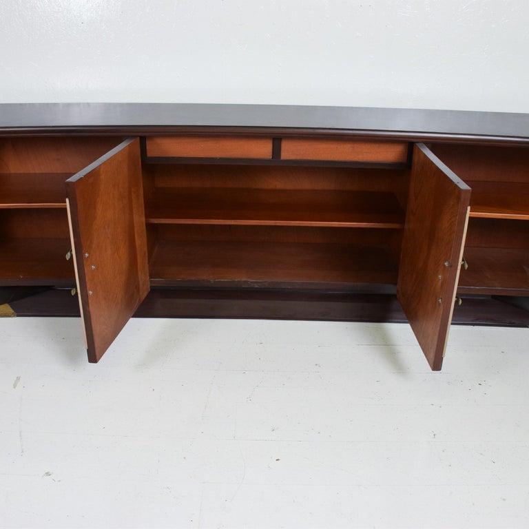 Stately long credenza by Arturo Pani. Unmarked. Made in Mexico 1950s
Custom sleek credenza in curved mahogany wood. Two tone presentation.
Center doors are covered in off-white creamy leather.
Magnificent brass pulls & sabots in original vintage