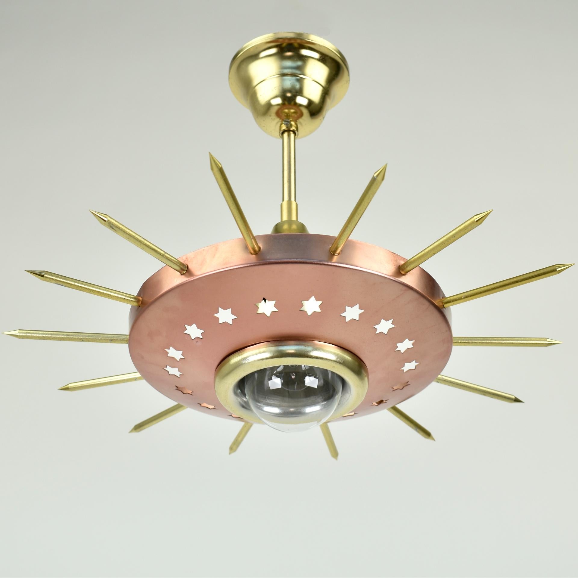 Very rare 1950s starburst ceiling lamp. This light has a copper colored aluminum shade with perforated stars, and gold colored starburst like rods.The lamp projects light spots on the ceiling trough the holes in the top.

Height: 28 cm /