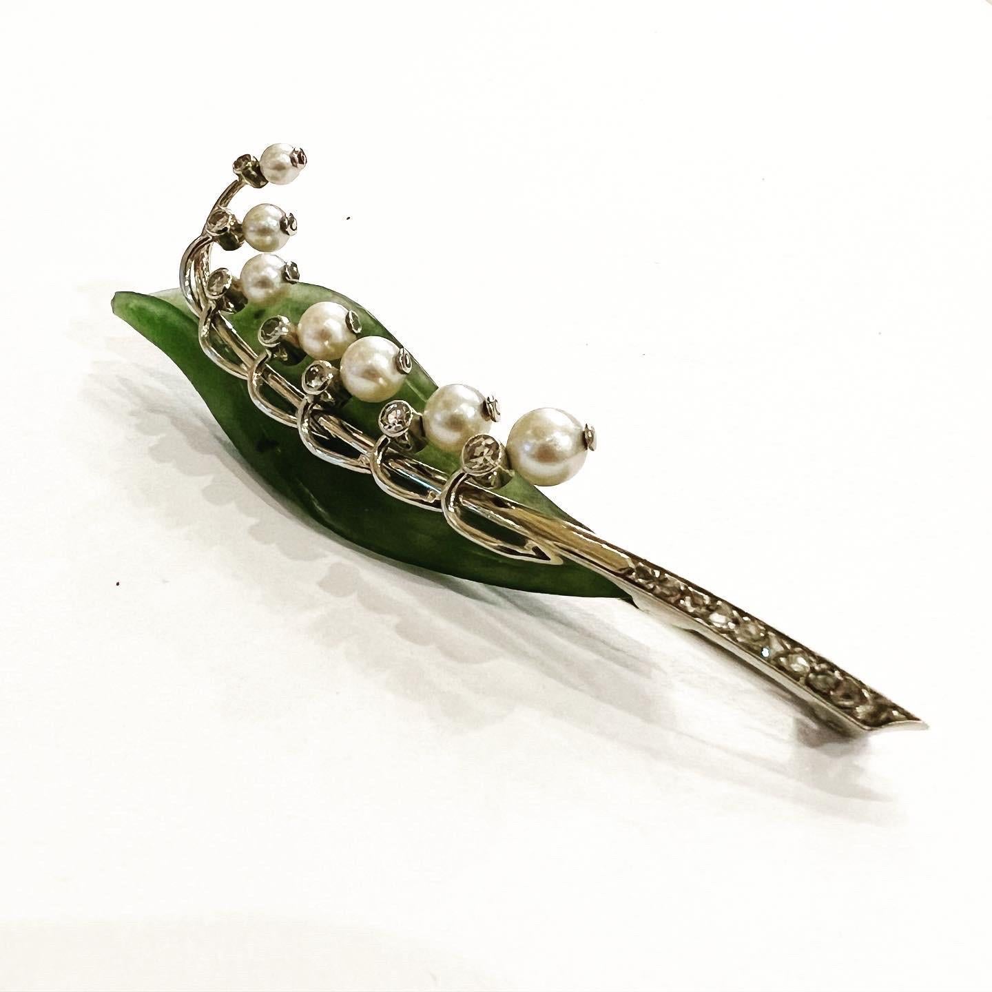 This amazing brooch is finely modeled as a beautiful Lily of the Valley.
The green leaf is naturalistically carved from a single piece of nephrite jade and as flowers there are pearls and diamonds.
The structure is made of 14K gold.  
Total aprox.