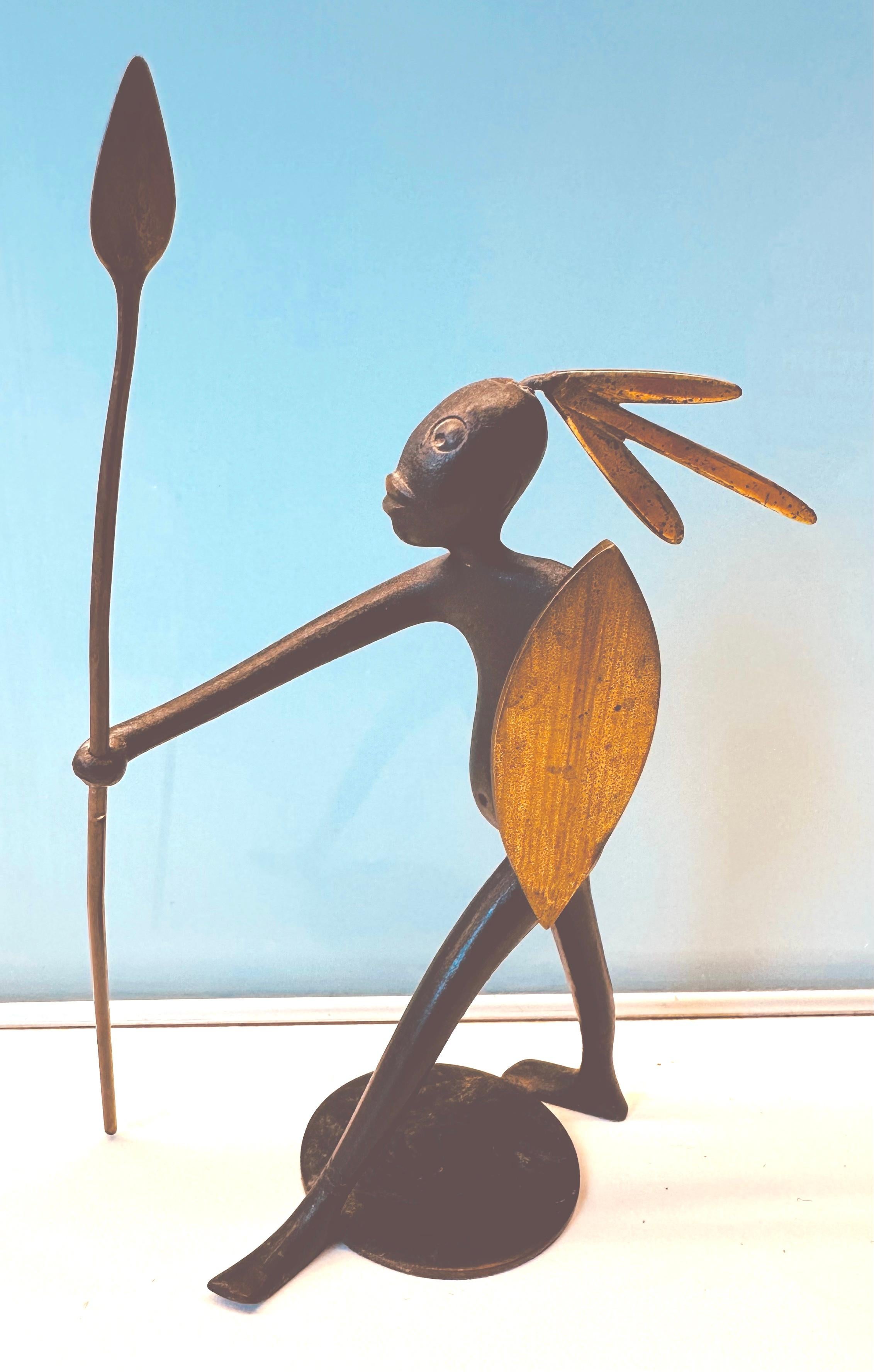 1950s, midcentury, black-patinated, bronze and brass figurine sculpture, of an African native warrior holding a shield and a spear with his arm fully-stretched. The warrior was designed and manufactured in Austria by Karl Hagenauer, Werkstätte