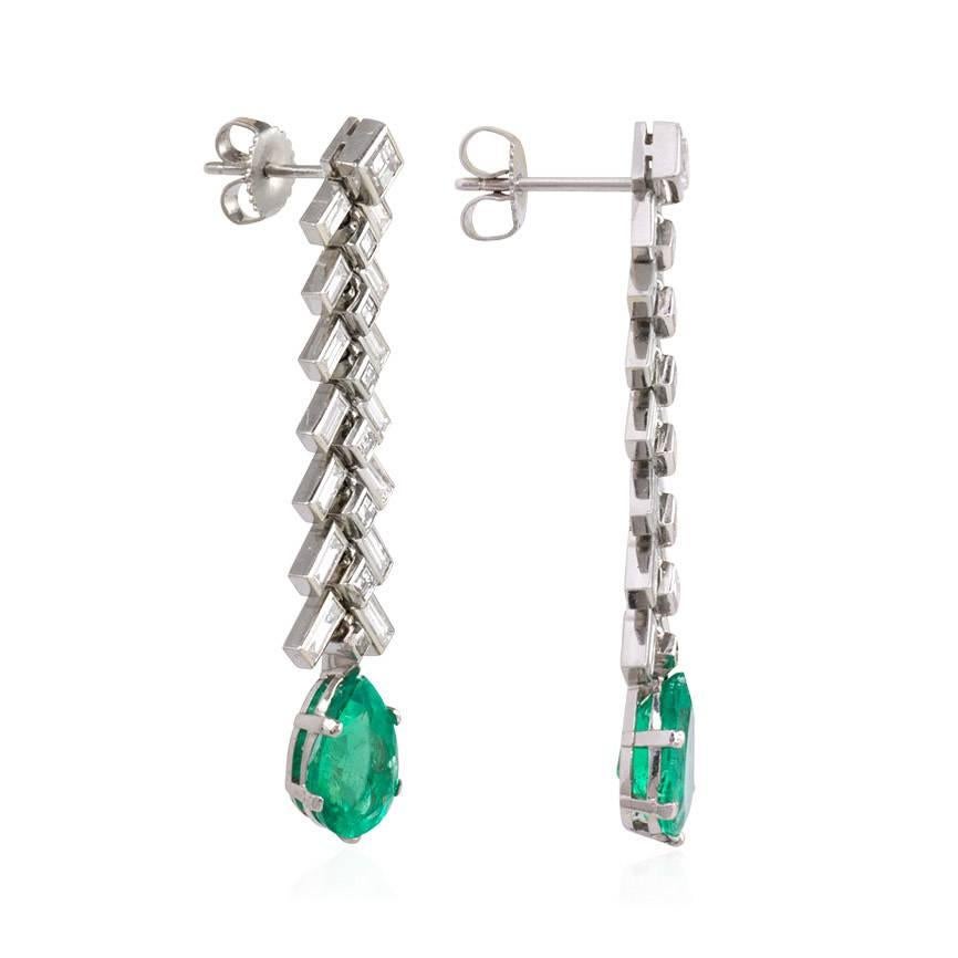 A pair of diamond pendant earrings designed as a line of chevroned baguettes terminating in a faceted pear-shaped emerald drop, in platinum. Emeralds approx. 1.58ct., 1.95ct.; atw. 3.00 ct. square step cut and baguette cut diamonds.