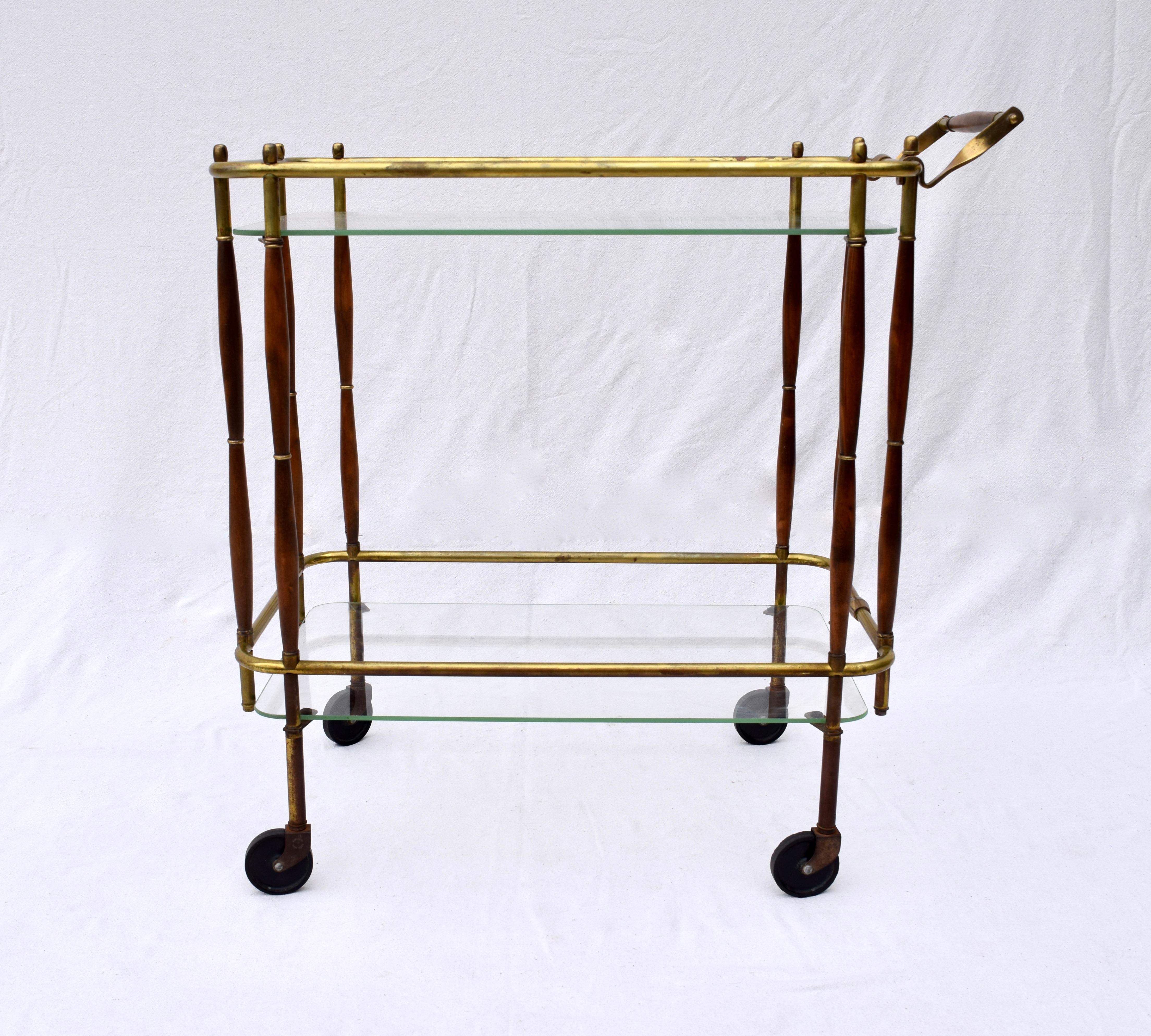 Midcentury bar cart of brass, walnut and two tiers of removable glass on casters, circa 1950. We have maintained the all original, beautifully patinated and tarnished finish in lovely vintage condition. Handle is 33.5 inches high.