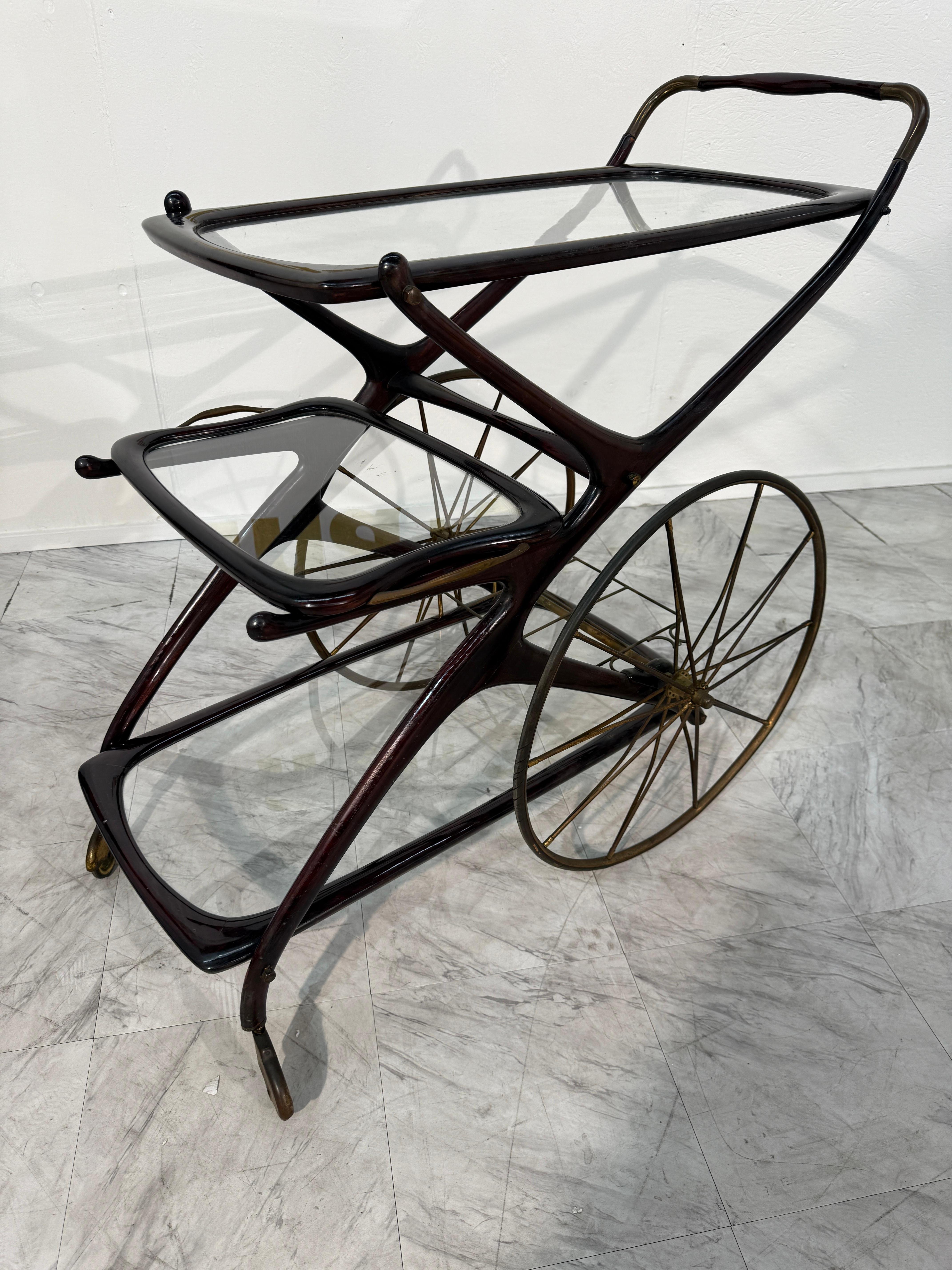 A sculptural marvel in motion, this vintage Italian bar cart glides effortlessly between function and fantasy. Crafted from richly stained wood, its sinuous frame curves with the elegance of calligraphy, echoing mid-century form and the whimsy of