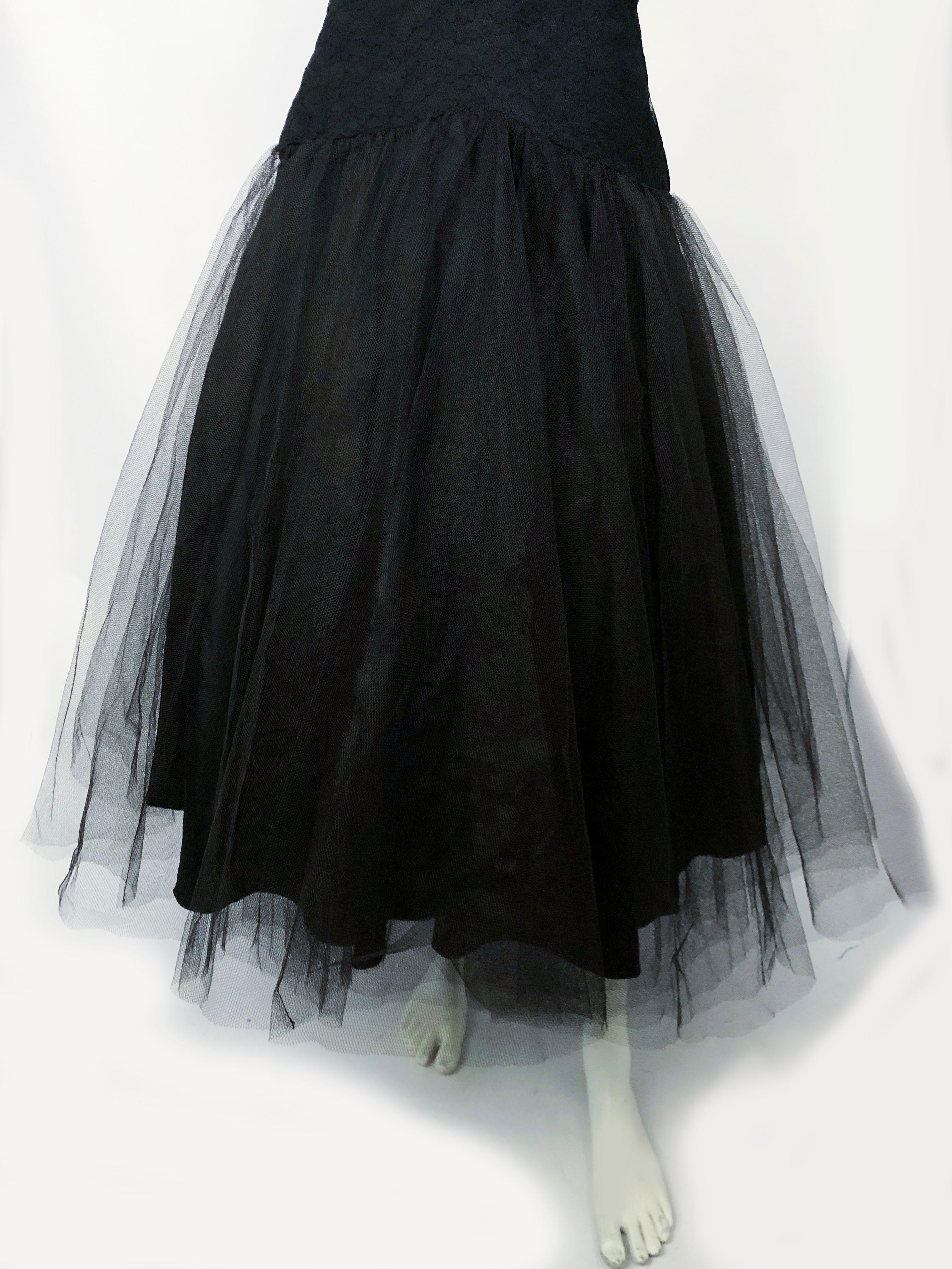 Black cocktail dress with a lace overlay on the bodes the is structured with layered racing and serves as a modesty panel. The drop-waist is accentuated by  a tule overskirt. The entire skirt is lined with a black taffeta. 