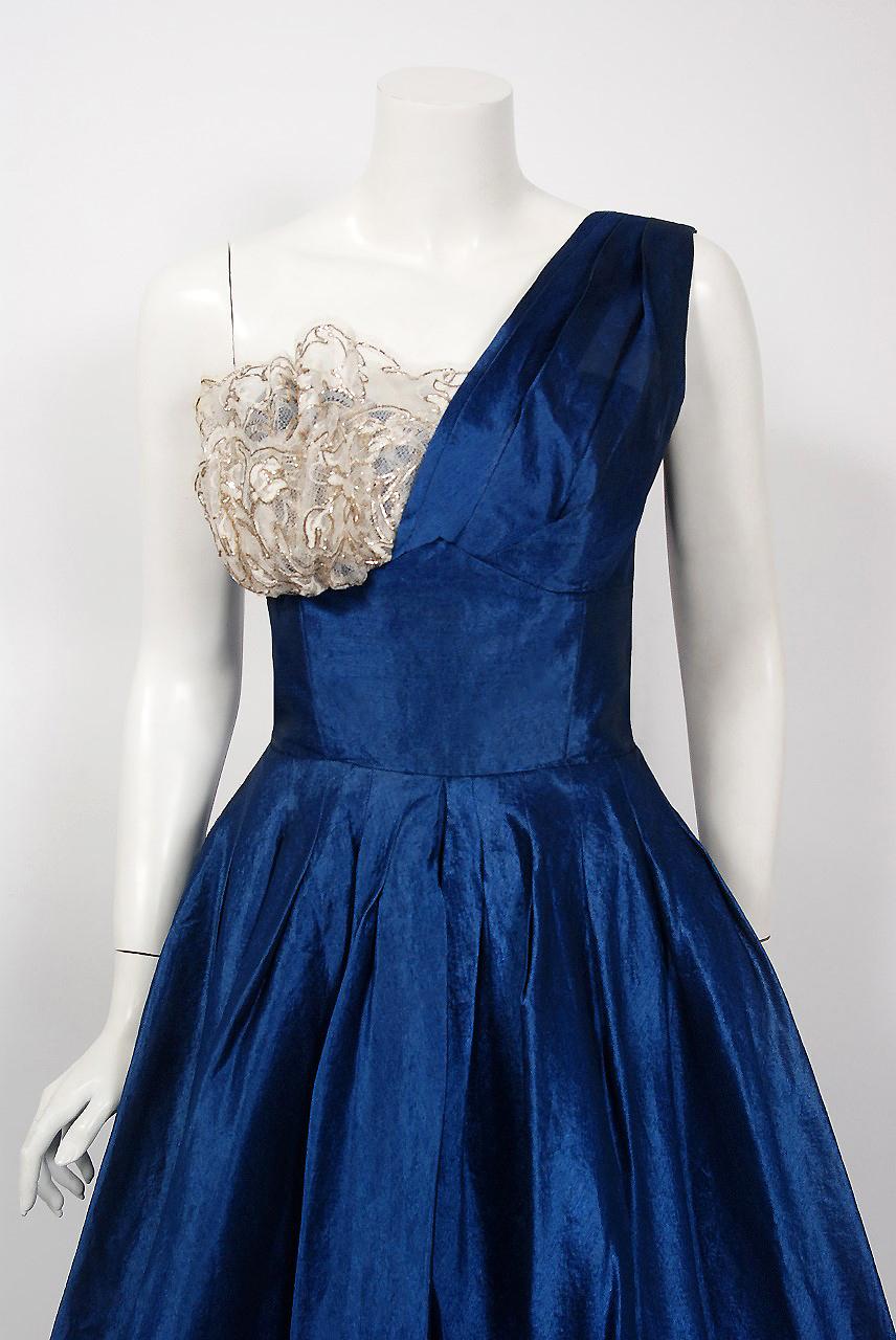 Fashioned from vibrant sapphire blue mid weight silk-organza, this 1950's Beaumelle creation has everything a woman wants. The bodice has a gorgeous ruched asymmetric one-shoulder shelf bust design. I adore the sparkling metallic threaded lace
