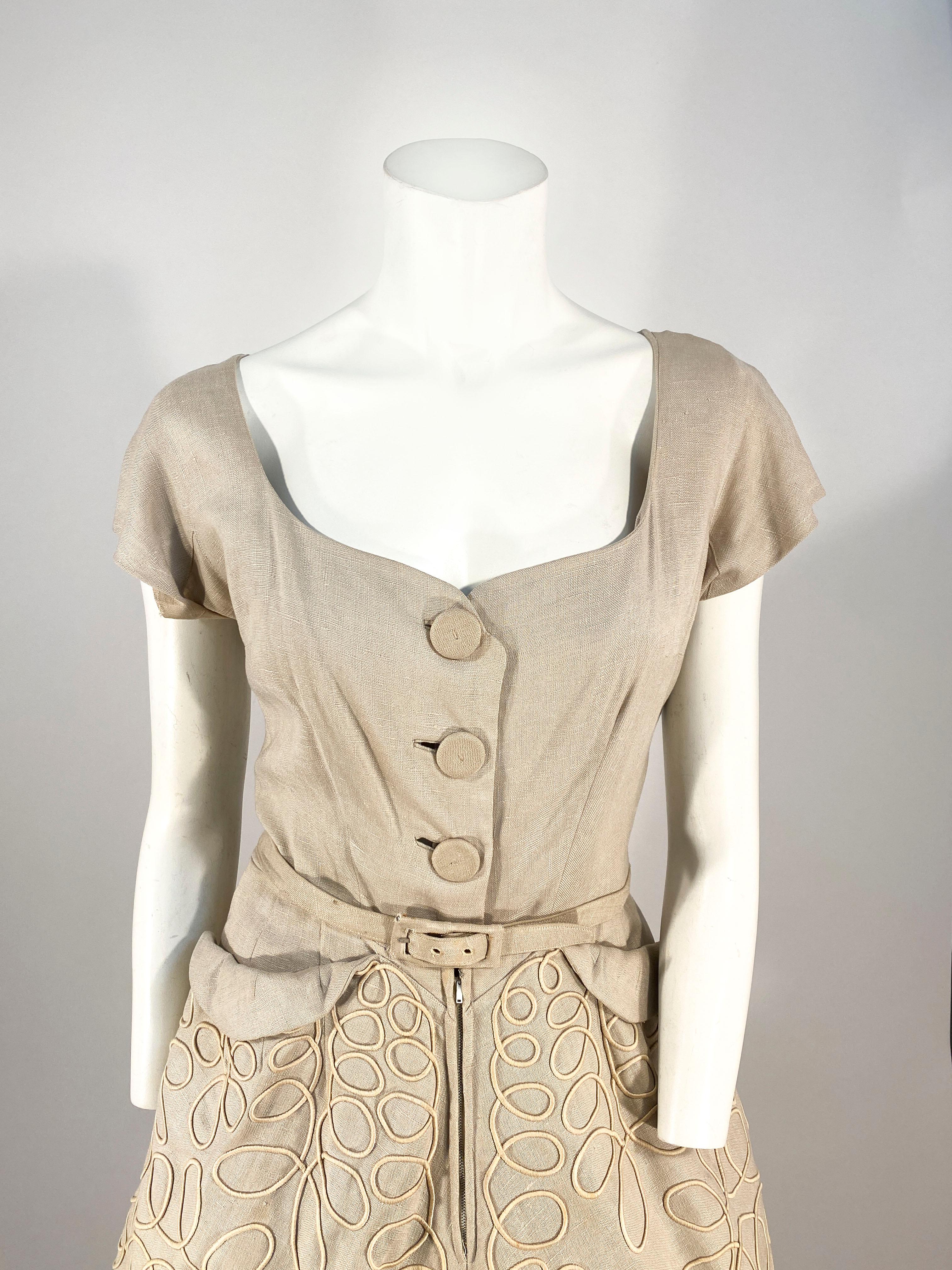 1950s Beige Linen day dress with a front covered button closure and a hidden zipper along the skirt. There is decorative lopped piping covering the entire surface area of the skirt. The bodice has short cap sleeves and a structured gusset and