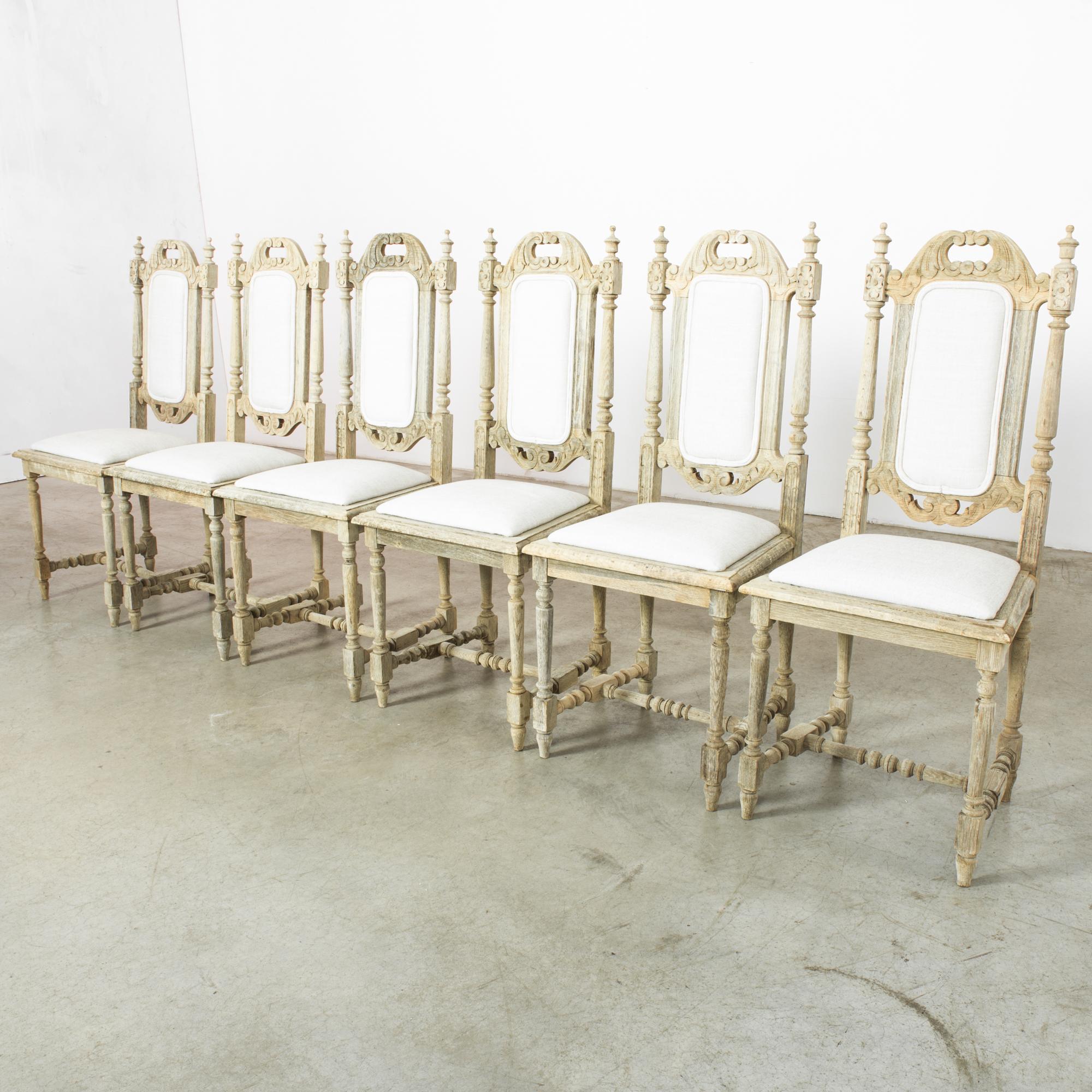 Genießen Sie die zeitlose Anziehungskraft eines Sets von sechs Stühlen aus gebleichter Eiche aus den 1950er Jahren, in denen das Design der Jahrhundertmitte auf königliche Eleganz trifft. Diese Stühle strahlen mit ihren weiß gepolsterten Sitzflächen