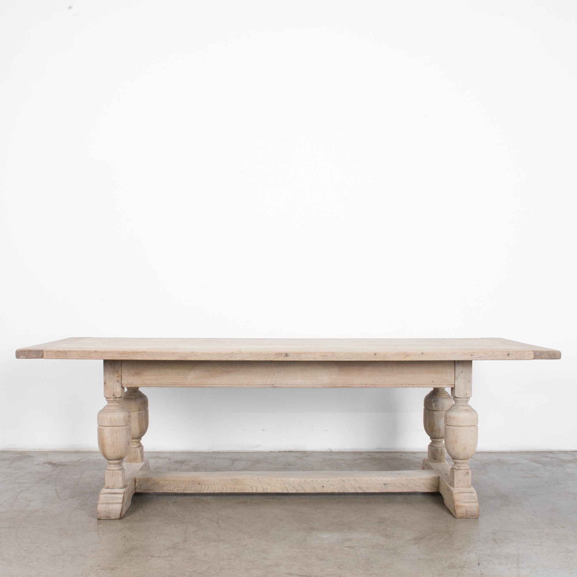 A bleached oak dining table from Belgium, circa 1950. A square tabletop, turned legs and a sturdy central strut create a farmhouse Silhouette. The heft and solidity of this table don’t impede its decorative charm, accentuated by the light finish of
