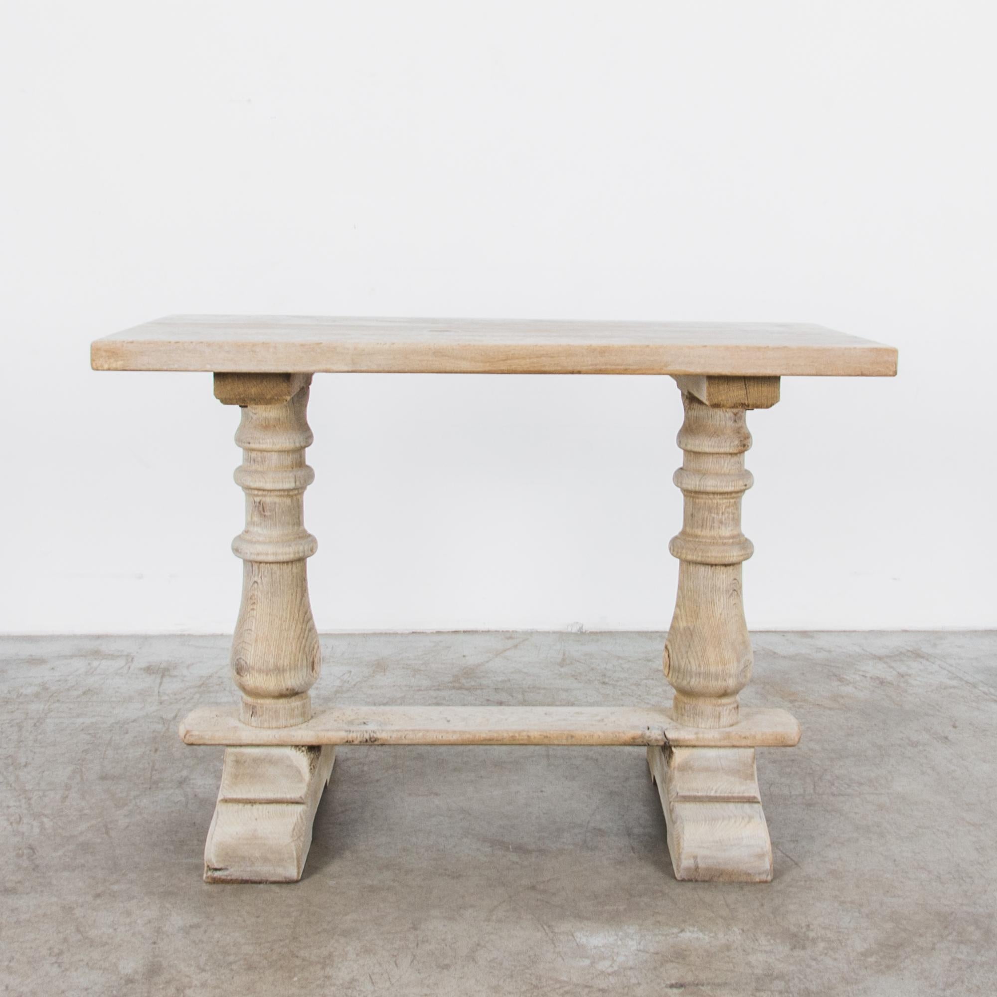 This oak trestle table was made in Belgium, circa 1950. Two sturdy turned oak legs joined by a stretcher support a simple tabletop, while a pair of sturdy scalloped braces elevate the whole. The wood has been restored to a bright bleached oak