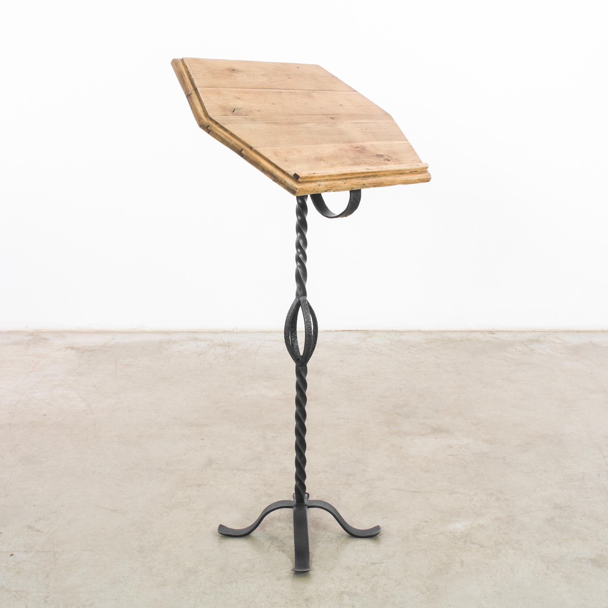 This 1950s Belgian iron book pedestal presents a unique fusion of rustic charm and functional design. The stand, crafted from wrought iron with a distinctive twisted design, culminates in a looped handle that adds an artistic flourish to its sturdy