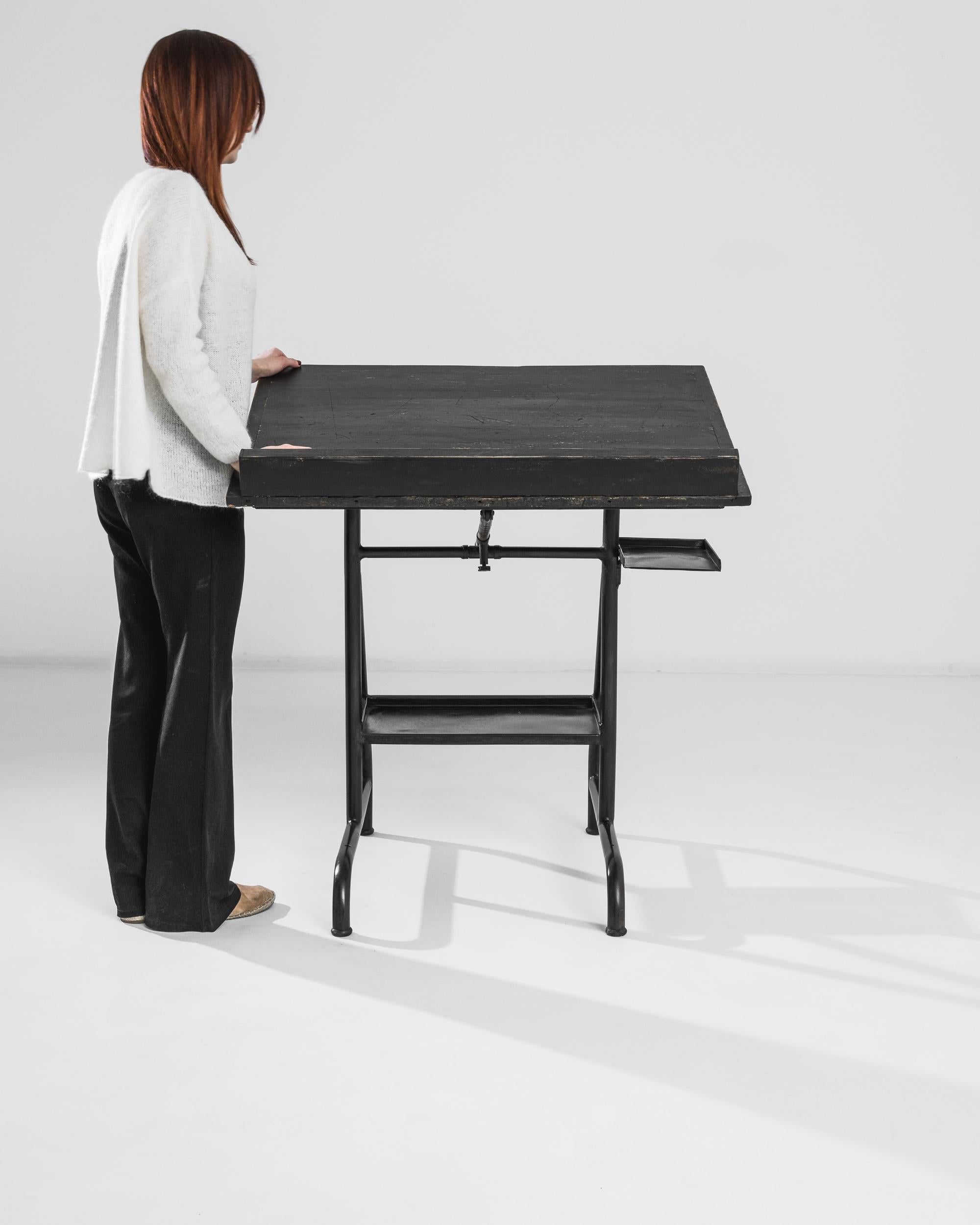 A metal drawing table from Belgium, produced circa 1950. Standing upon a sleek tubular frame, the articulated wooden top of this drawing table swings up and down to give the user the optimal angle for drafting. Features a small upper shelf and