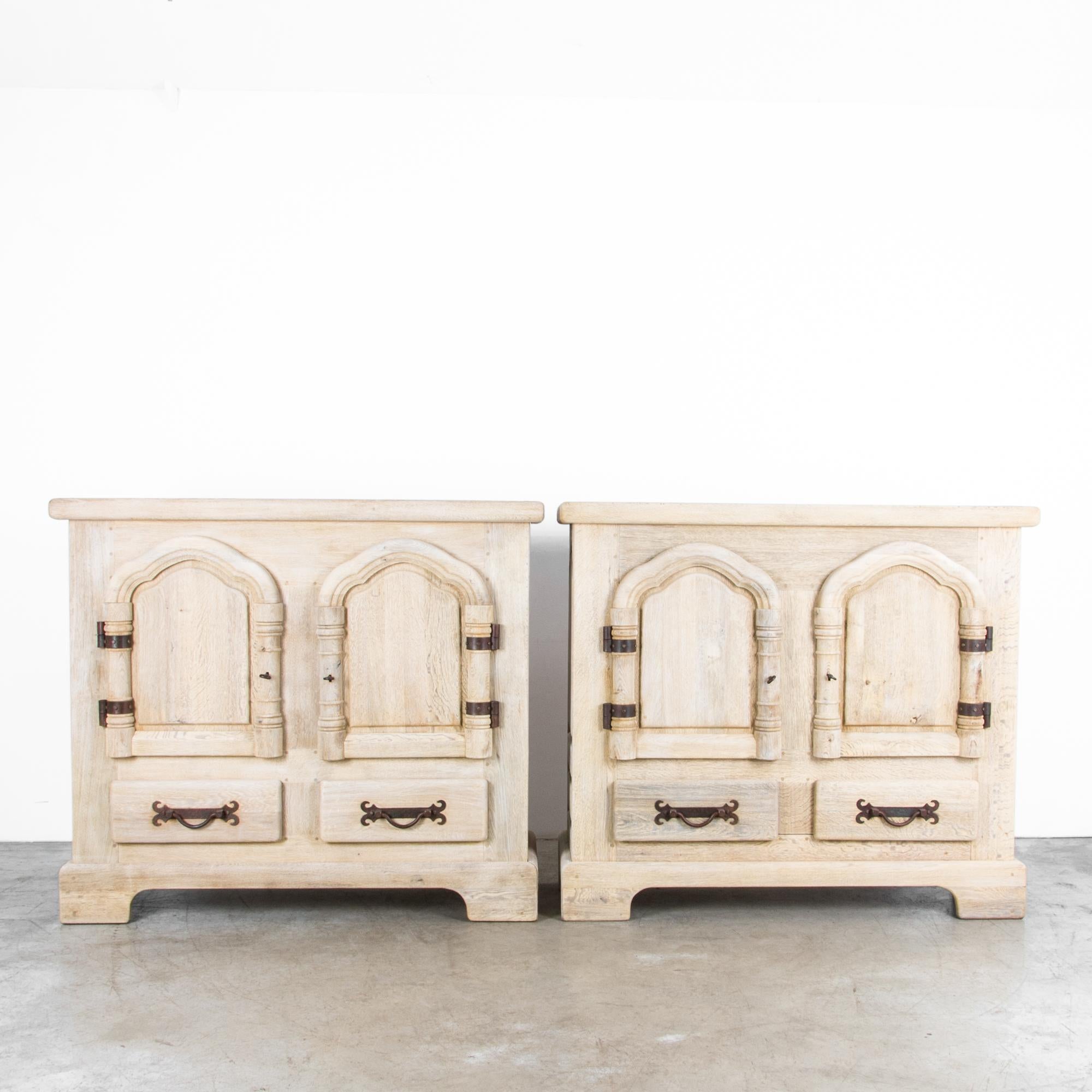 A pair of oak buffets from Belgium, circa 1950. Each cabinet features two doors and two lower drawers, with fixed interior shelves. A simple case is enlivened by the Gothic influenced arches of the doors and the decorative ironwork of the hinges and