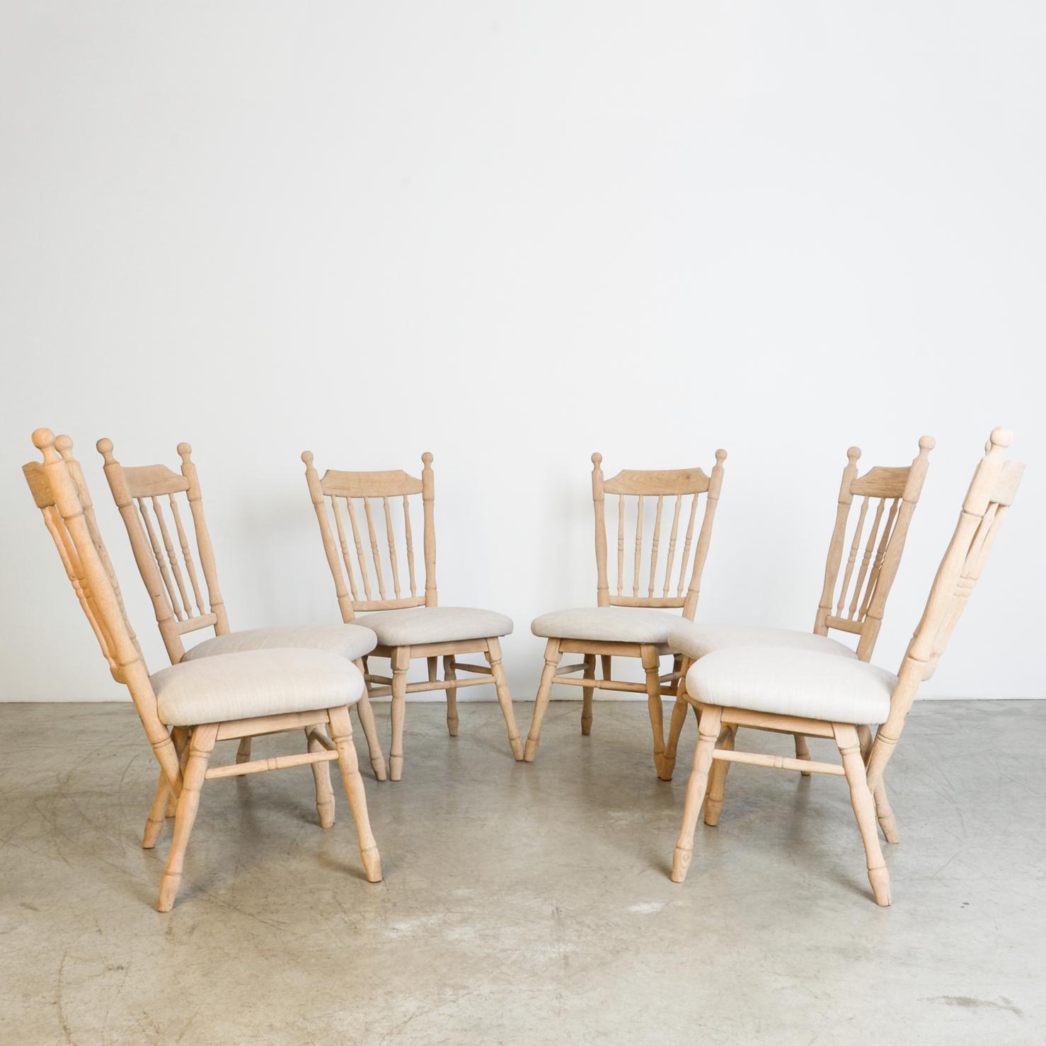 From circa 1950 Belgium, these sturdy oak chairs are influenced by classical furniture styles, seen through a simplified, mid-20th century lens. A casual country shape is composed of decorative turned spindles and formal legs in late rendition of