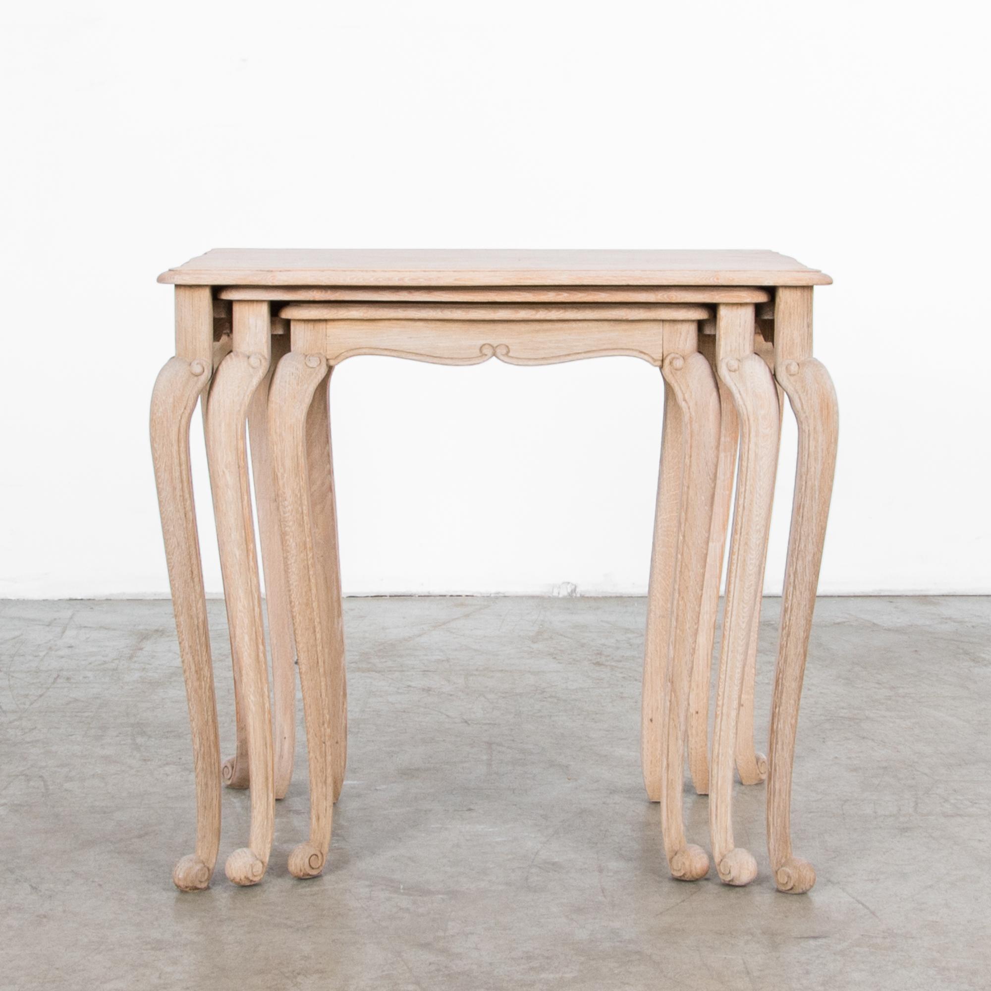 Made of bleached oak, this set of three nesting tables hails from Belgium, circa 1950. Slender cabriole legs feature a subtle scroll, supporting an embellished tabletop with a graceful symmetrical apron. The understated finish of the wood gives