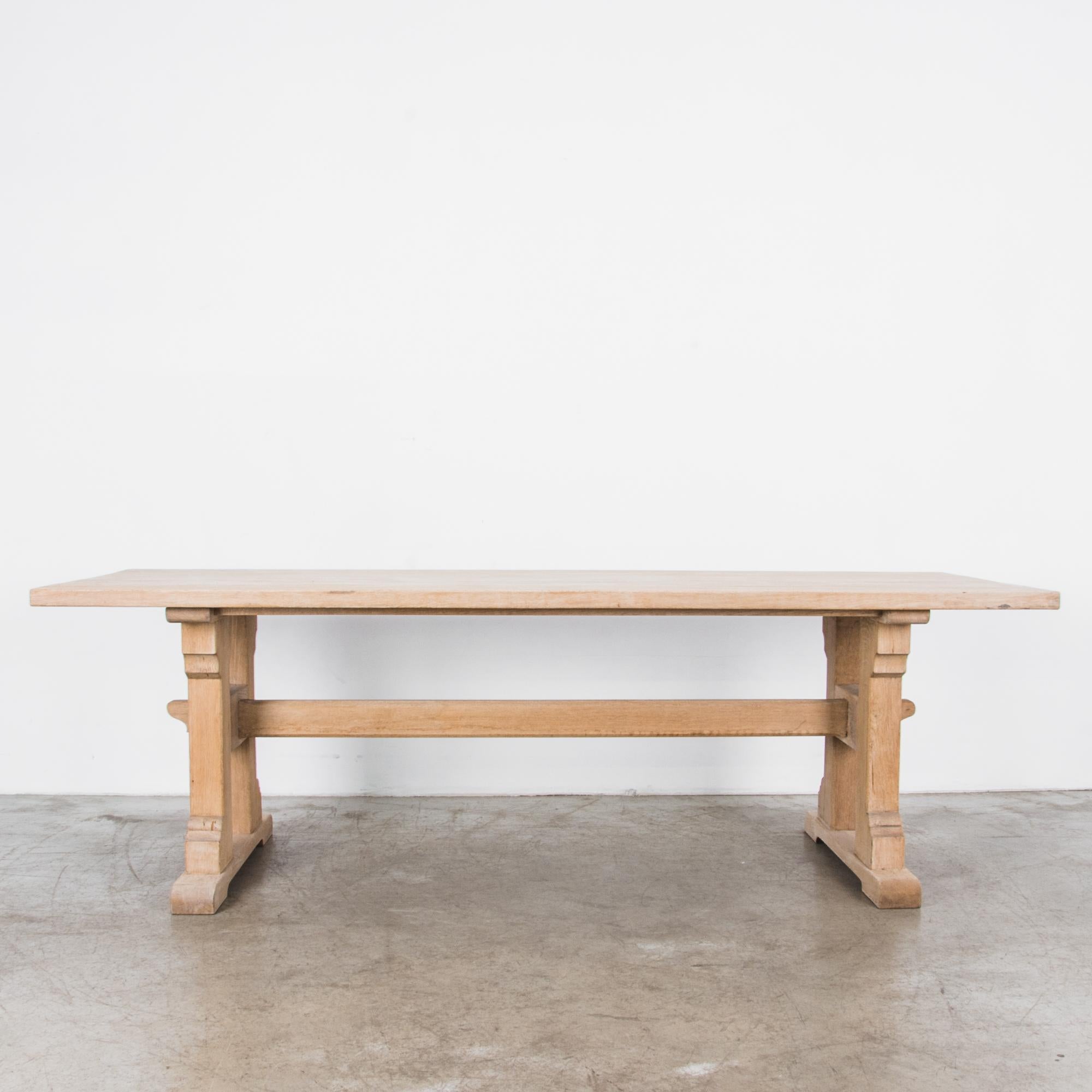 An oak trestle table from Belgium, circa 1950. A striking H-shaped leg construction atop a pair of rounded braces supports a long tabletop, measures: 95”. The legs are joined by a trestle and held in place with wooden pins, a design that is both