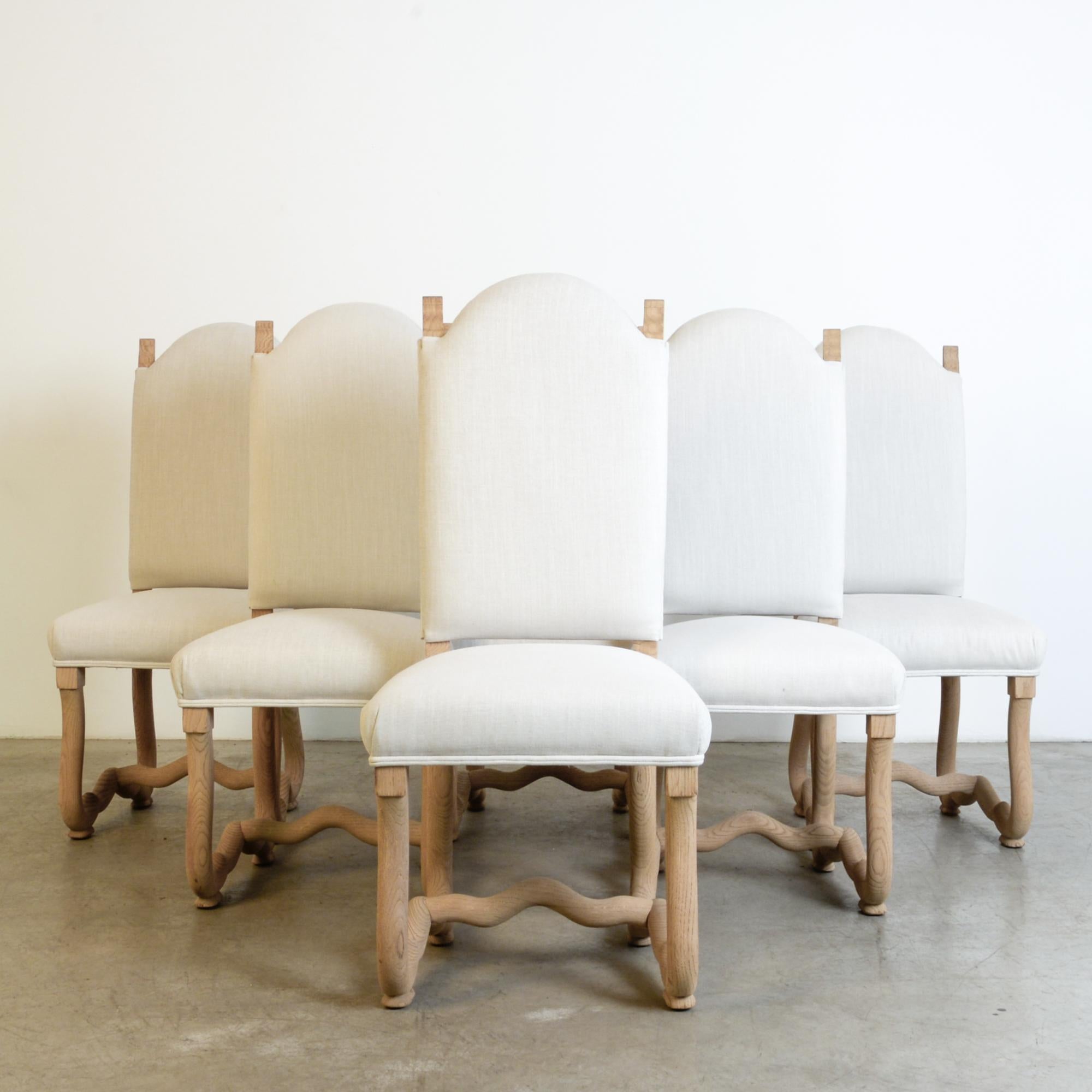 From circa 1950 Belgium, these oak dining chairs re-interpret the traditional “Os de Mouton” decorative motif. These “sheep bone” chairs have a distinctive curve, here seen in the lower frame of the chair. An elegant ornamental form, seen through a