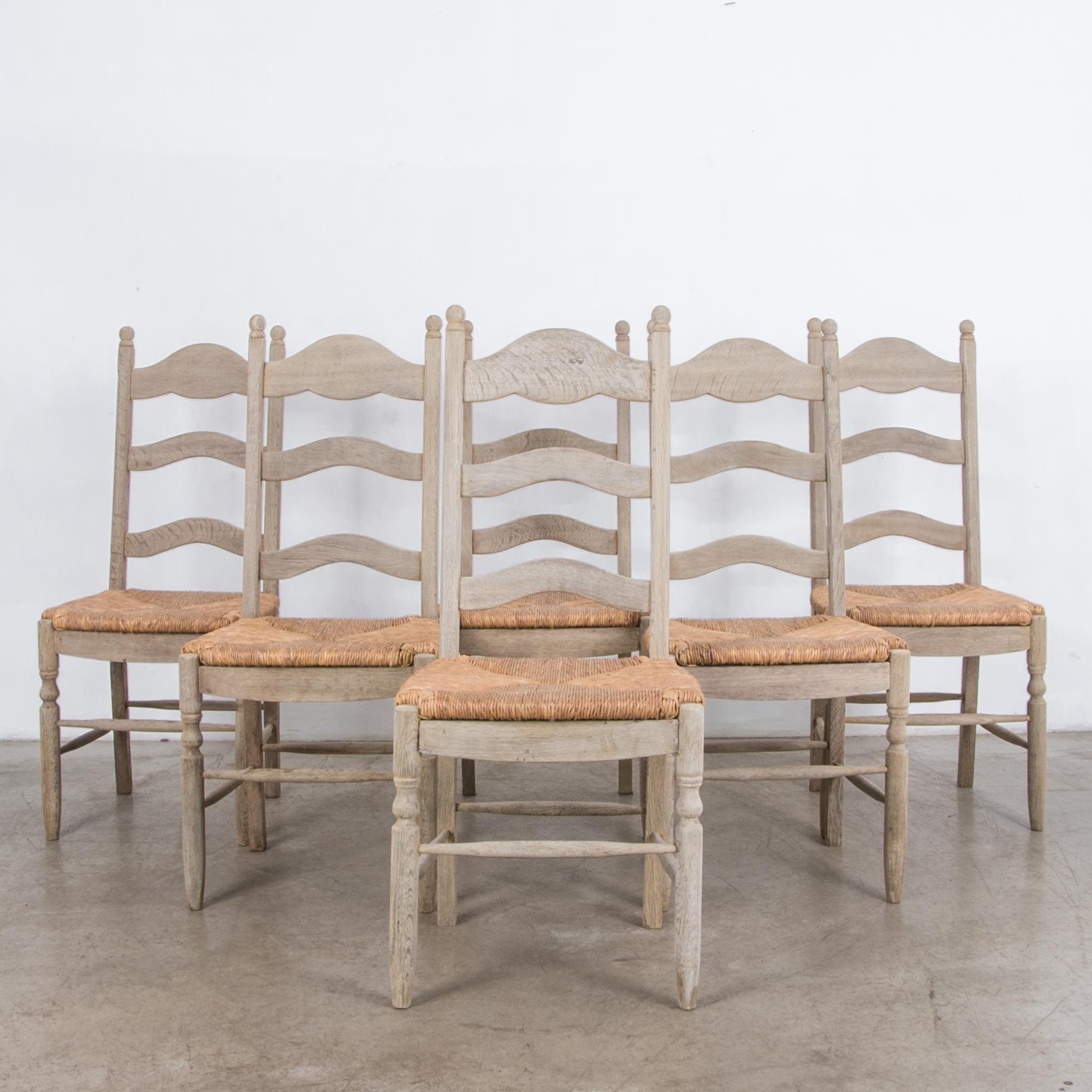 From Belgium, circa 1950, this set develops the form of the traditional oak dining chair seen through a simplified mid-20th century modernist lens. With clear oil and wax finish and hand twisted rush seat, a natural color palette and homage to the