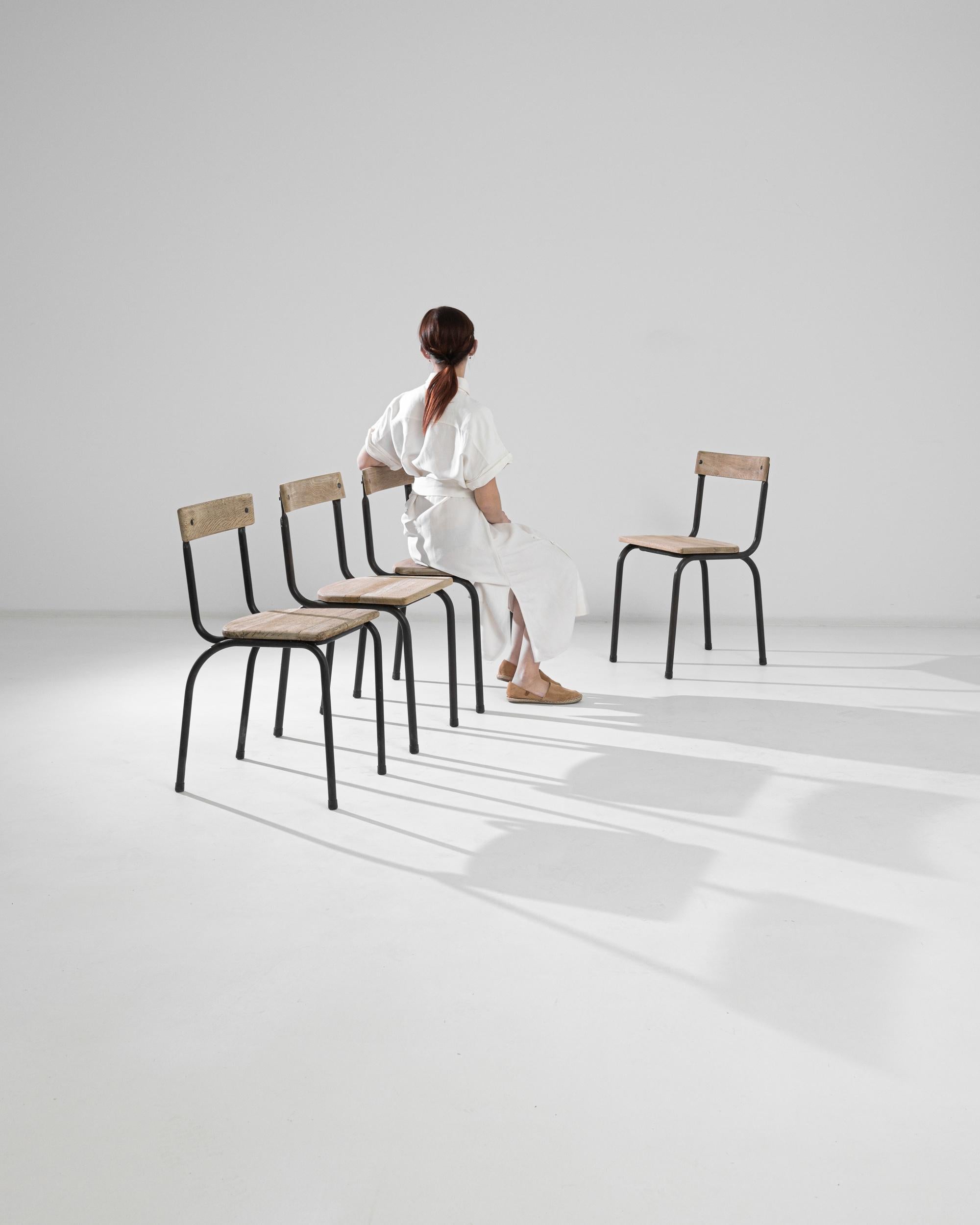 Fabriqué en Belgique vers 1950, cet ensemble de quatre chaises en métal dégage un air de Bauhaus. Fonctionnels et élégants, ils comportent une base tubulaire en métal qui supporte des sièges et des dossiers en bois. Le noir industriel du métal se