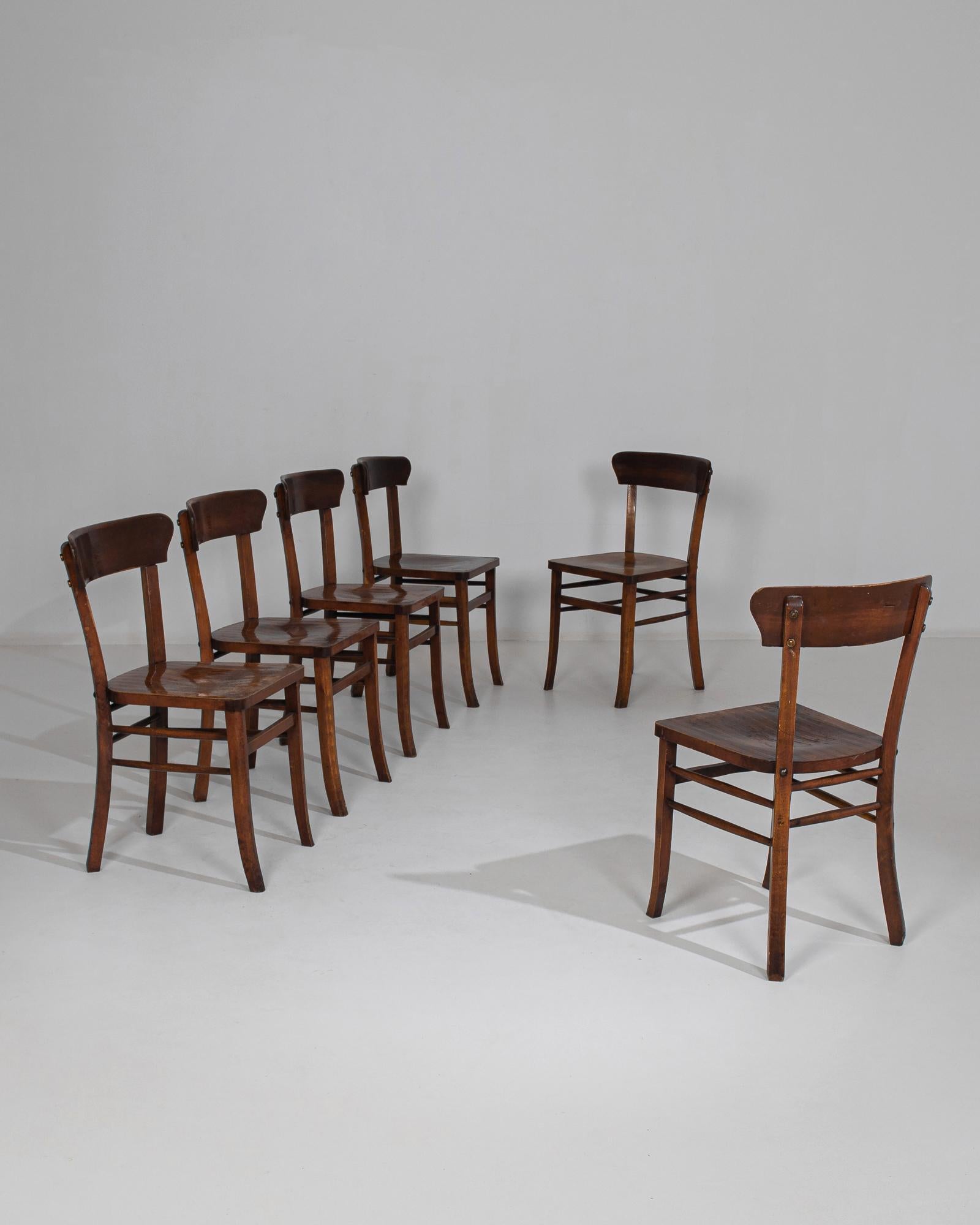 This set of six wooden dining chairs was made in Belgium, circa 1950. The streamlined design highlights the chairs' subtle features, from the gentle indentation on the seats to the curves of the splayed legs and top rail. Beautifully weathered with