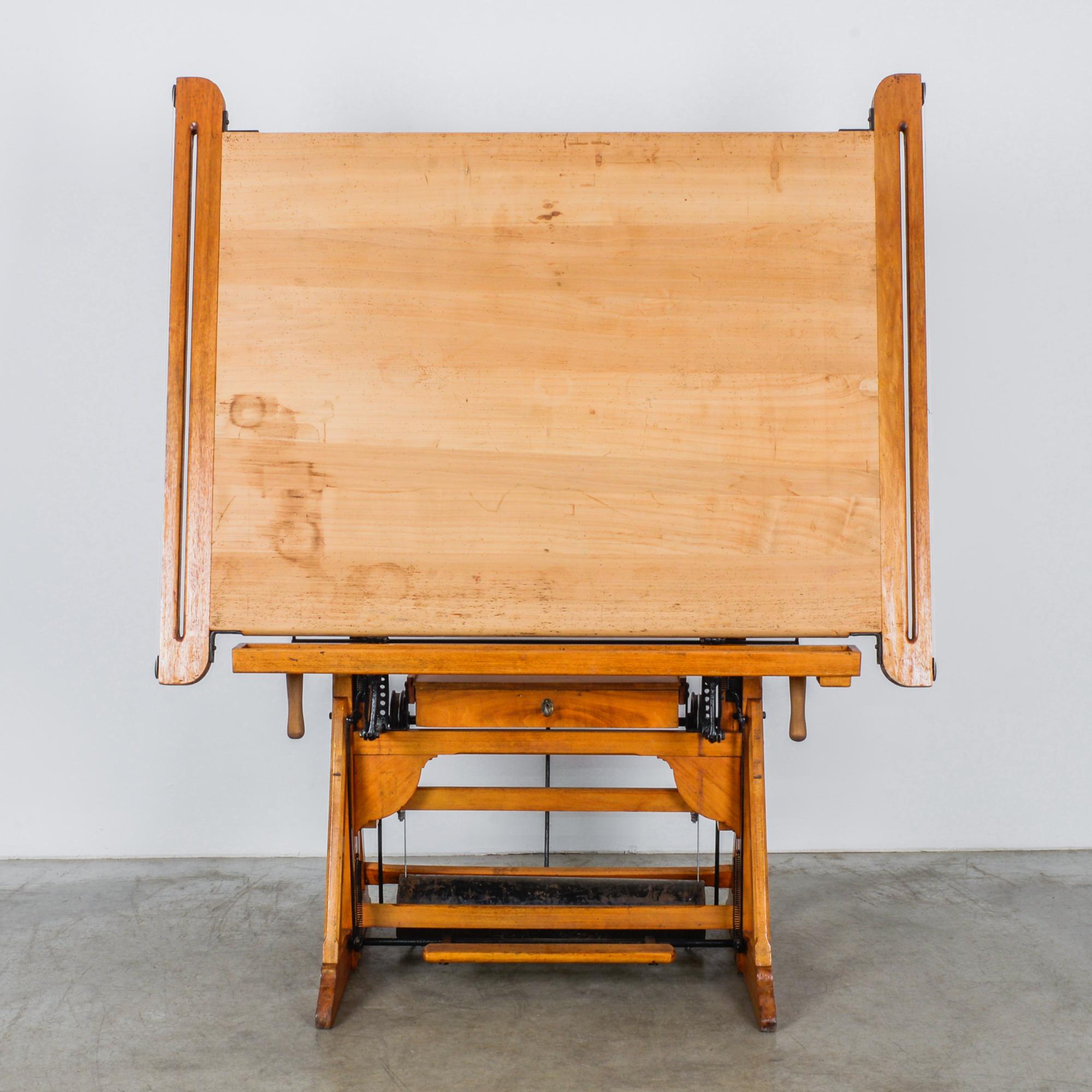 A wooden drawing table from Belgium, circa 1950. An intricate mechanical construction allows the broad tabletop to be raised, lowered and angled to a horizontal or vertical position, allowing the draftsman to work sitting or standing up. A-frame