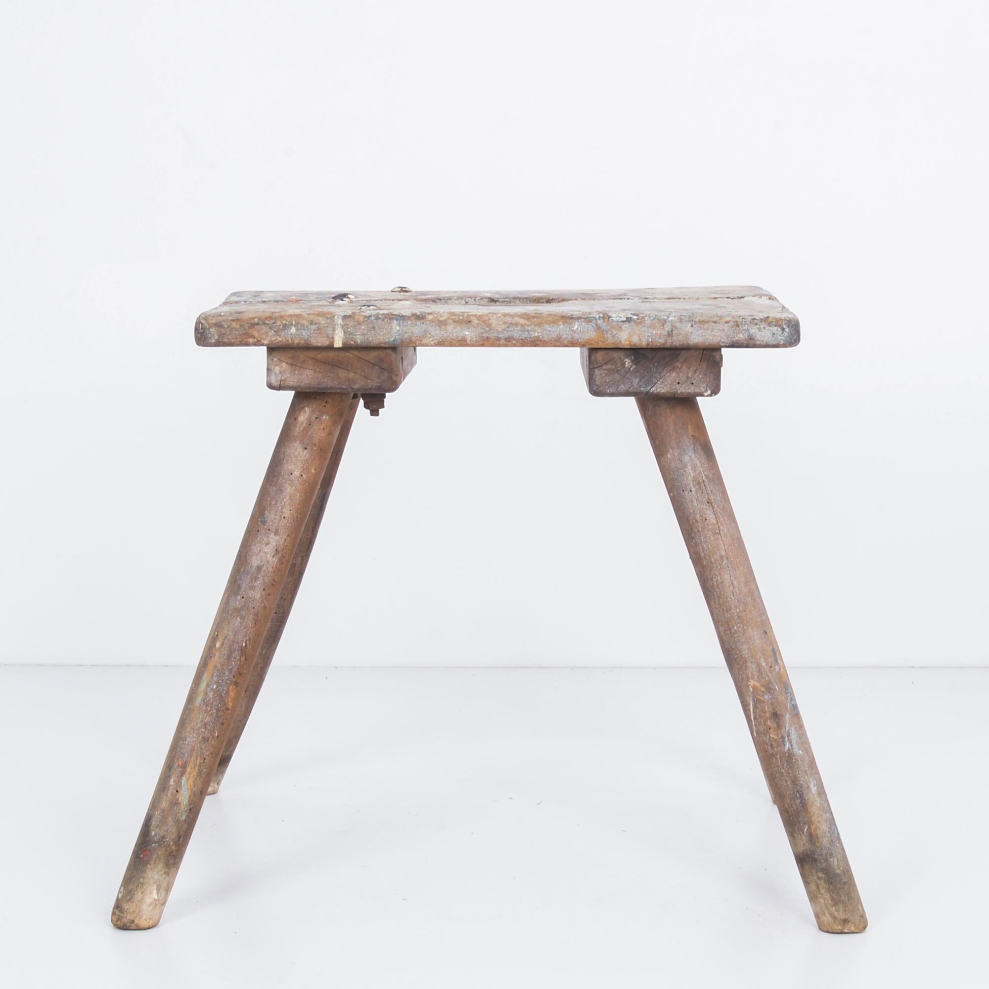 A wooden workman’s stool from Belgium, circa 1950. Four splayed legs support a worn rectangular seat, streaked and spattered with paint. This soft, irregular patina, with variegated grey and white tones, is evocative of this piece’s history of use.