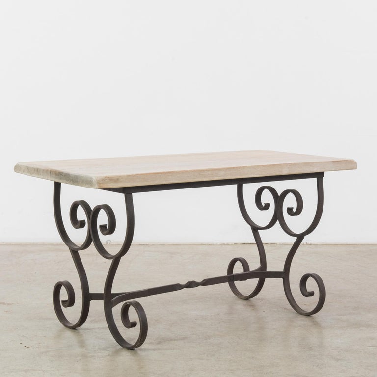A 1950s table from Belgium. A wrought metal frame of bold curlicues supports a simple tabletop; the flourishes of the metal make a striking contrast with the soft corners and natural finish of the wooden slab. Graphic and whimsical, a romantic